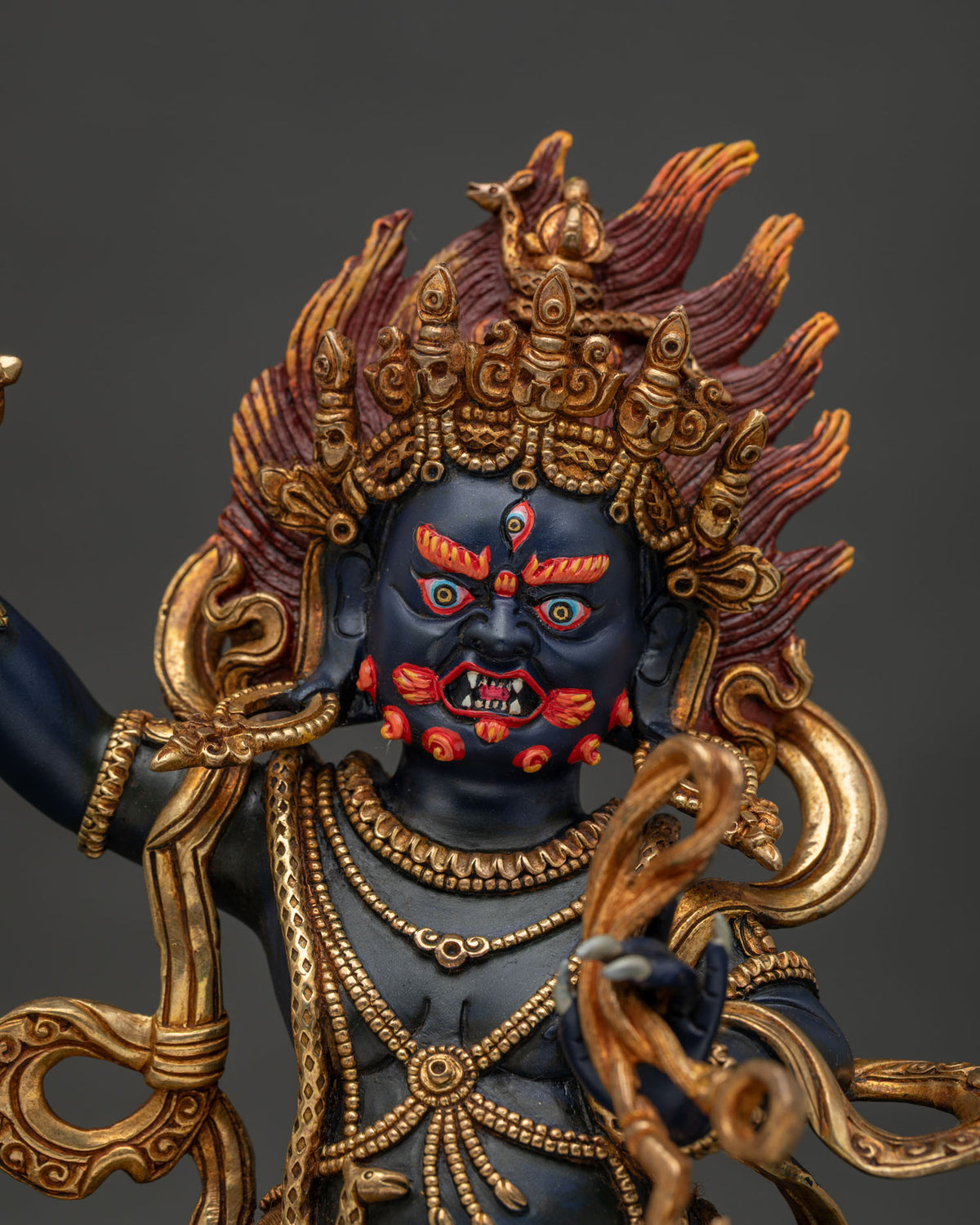 Close up of gold-gilded Vajrapani sculpture showing the vajra, lasso and vibrant details.