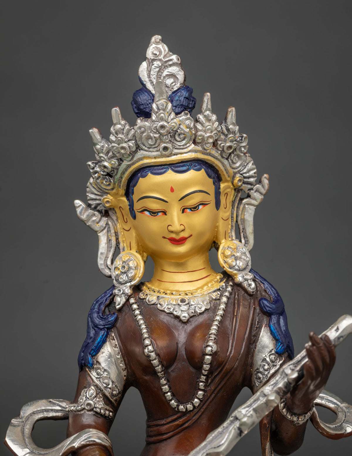 Close-up of gold-painted face and silver crown on oxidized copper Saraswati statue from Nepal