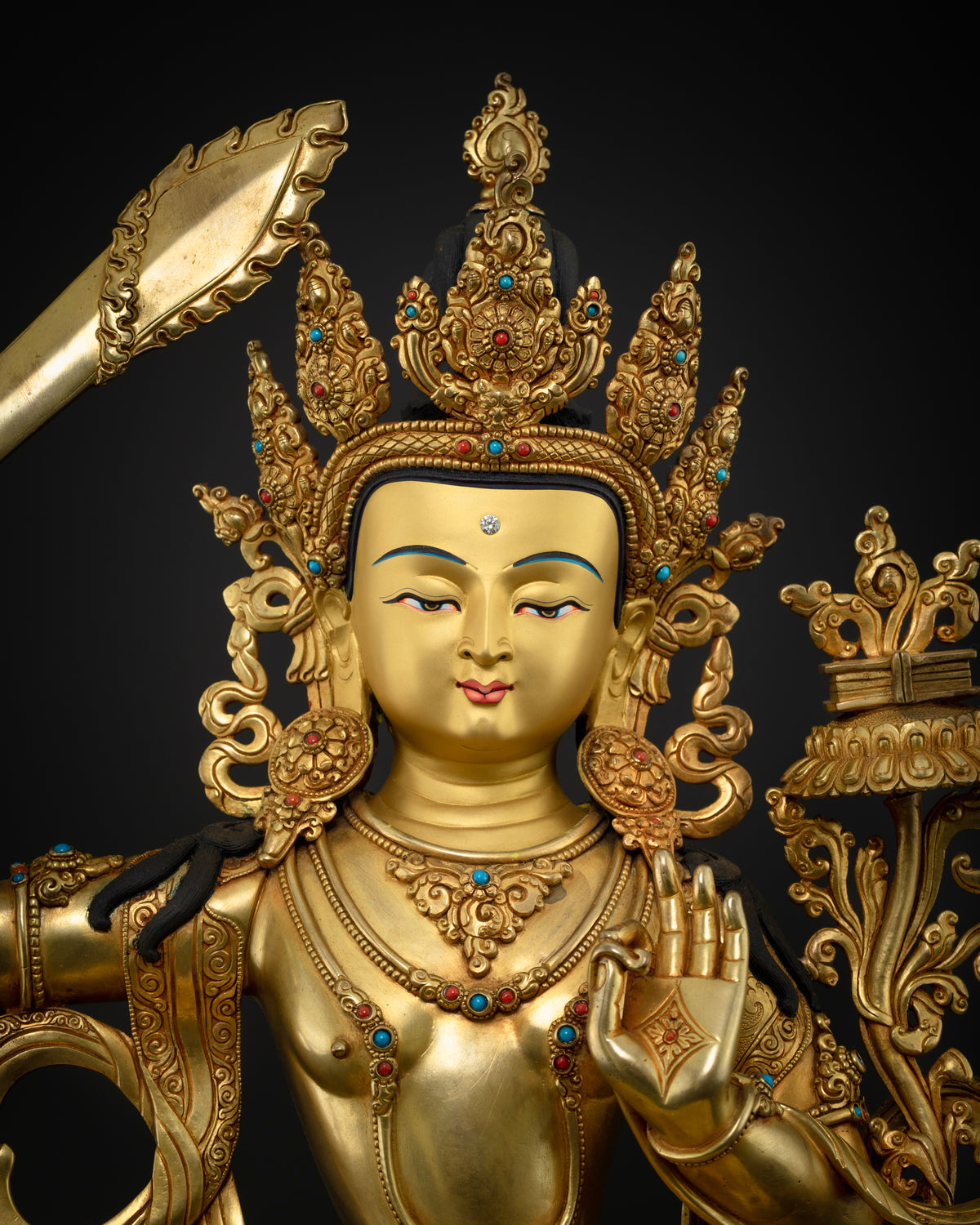 Close-up of gold-painted face with ornate crown, turquoise and coral jewelry on Manjushri statue