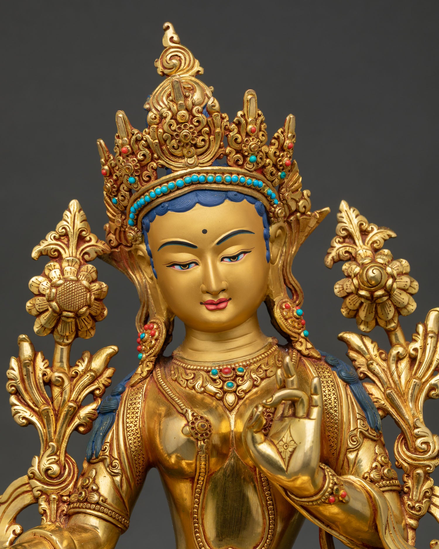 Close up of Green Tara Statue, showing gold painted face serene expression and intricate gemstone ornaments