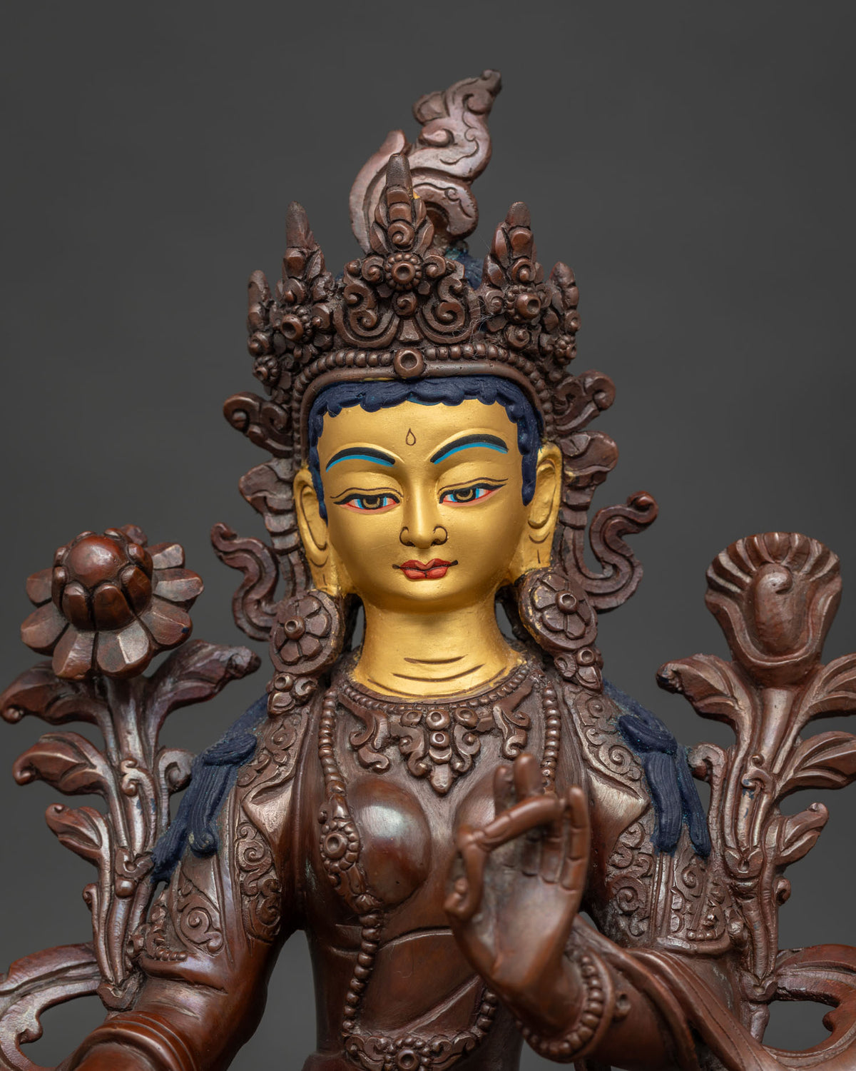 Close up of Green Tara statue with five jeweled crown and sacred utpala flower.