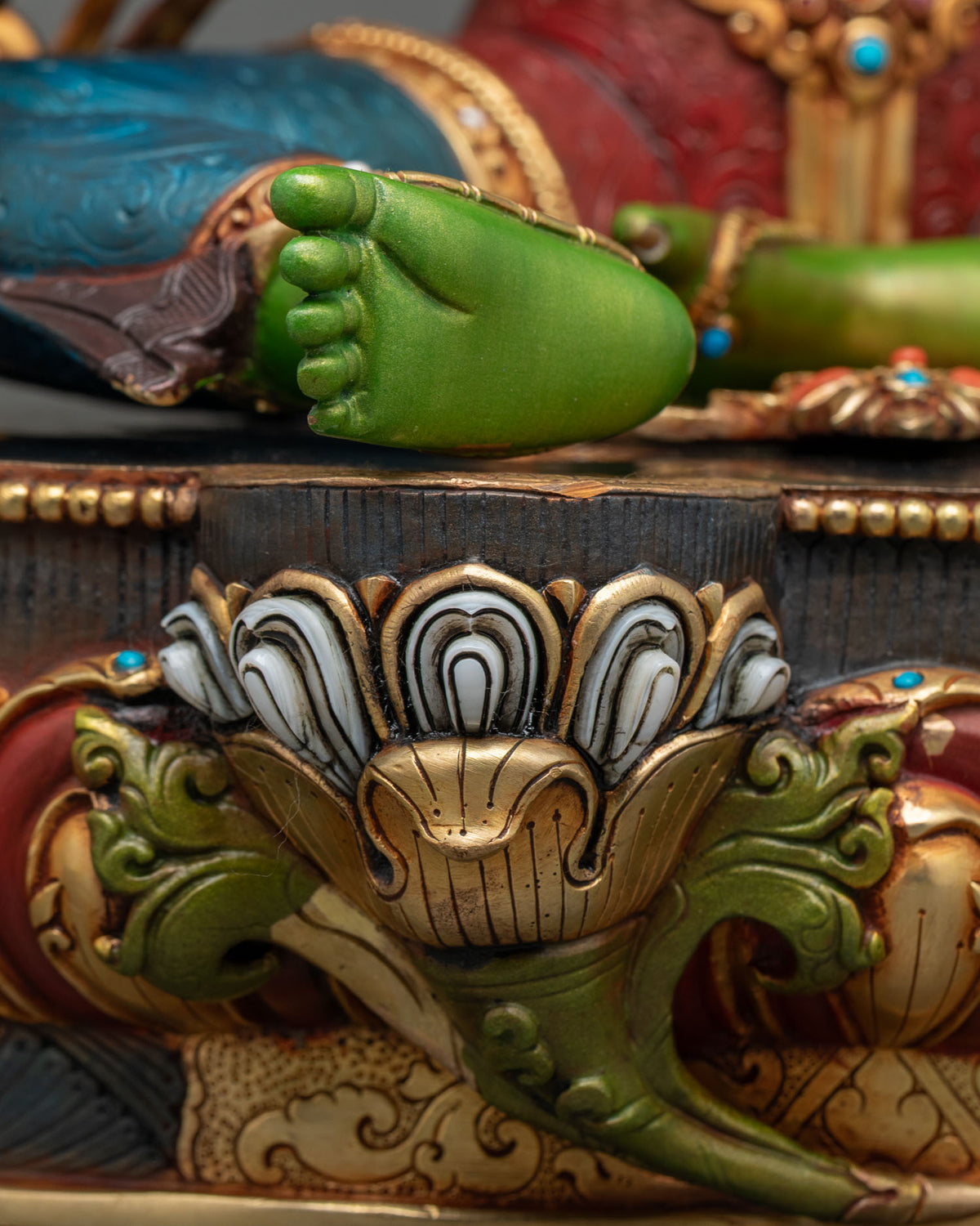 Close-up of Green Tara’s bare foot and carved lotus pedestal with white and gold petals