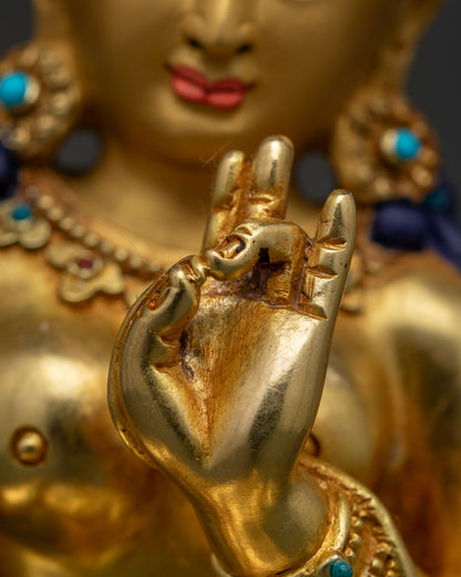 Close-up of Green Tara's hands near heart in abhaya mudra with gold jewelry detail