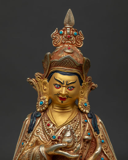 Close up of Guru Rinpoche face with red lotus hat vulture feather and gold gilded details.