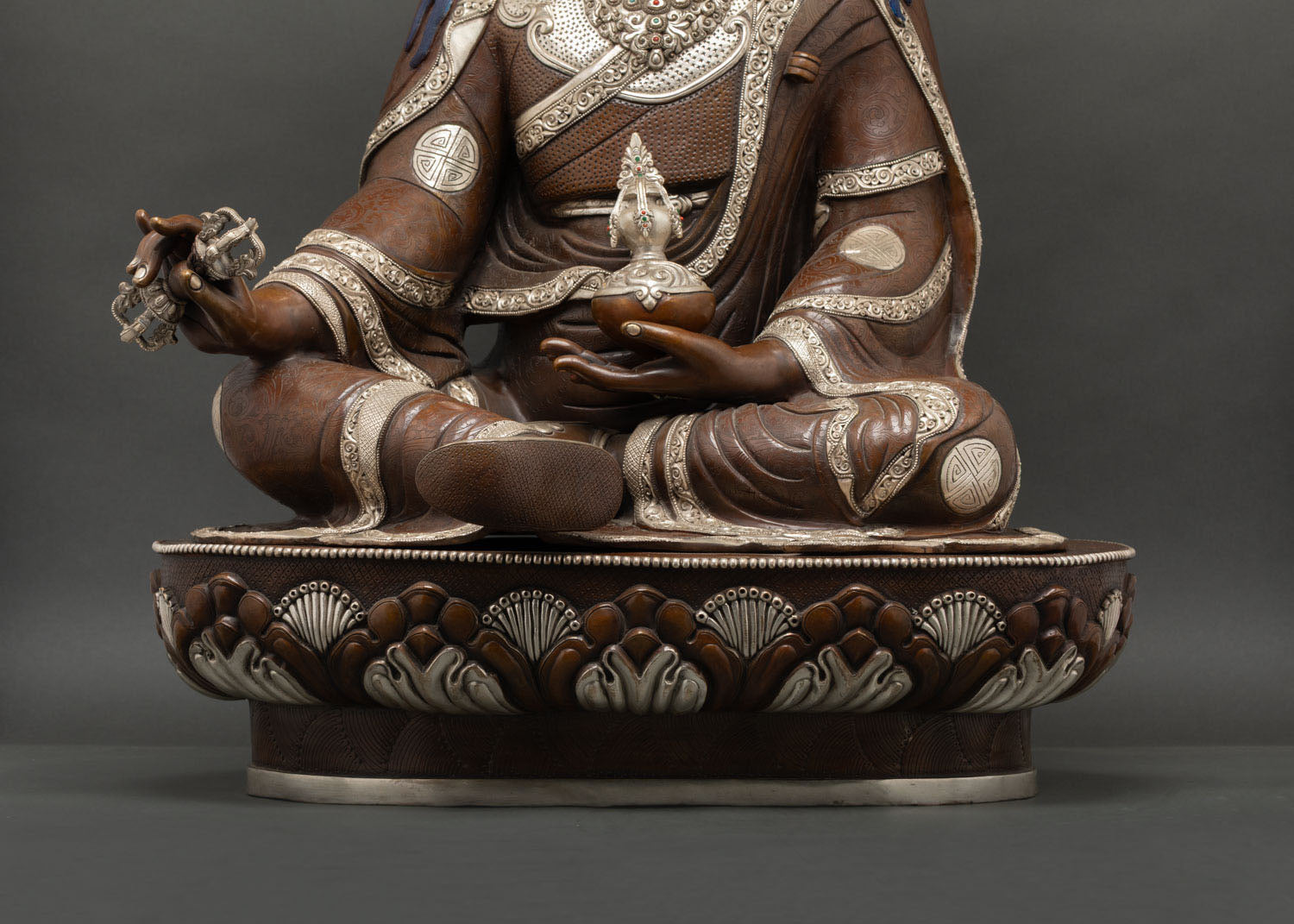 Close-up of Guru Rinpoche hand holding a silver-plated vajra with hand-chased carving.