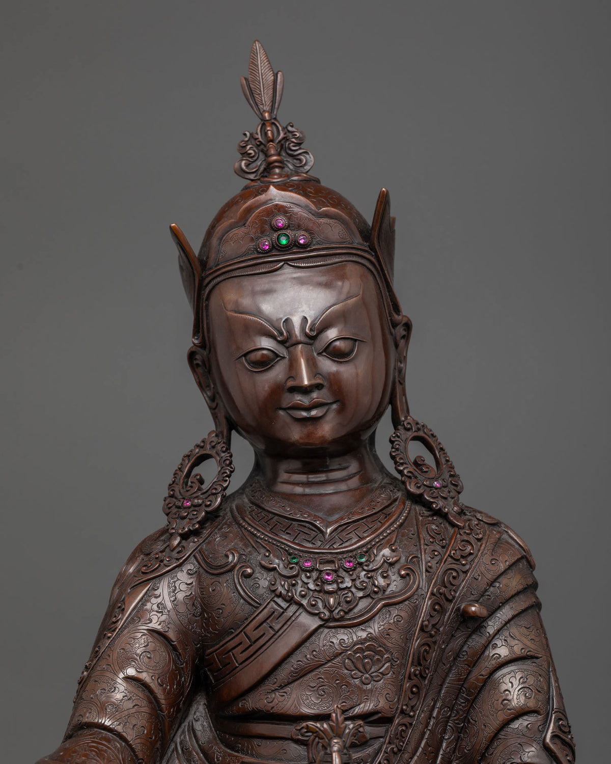 Close-up of Guru Rinpoche statue face, jeweled lotus hat and engraved copper robes