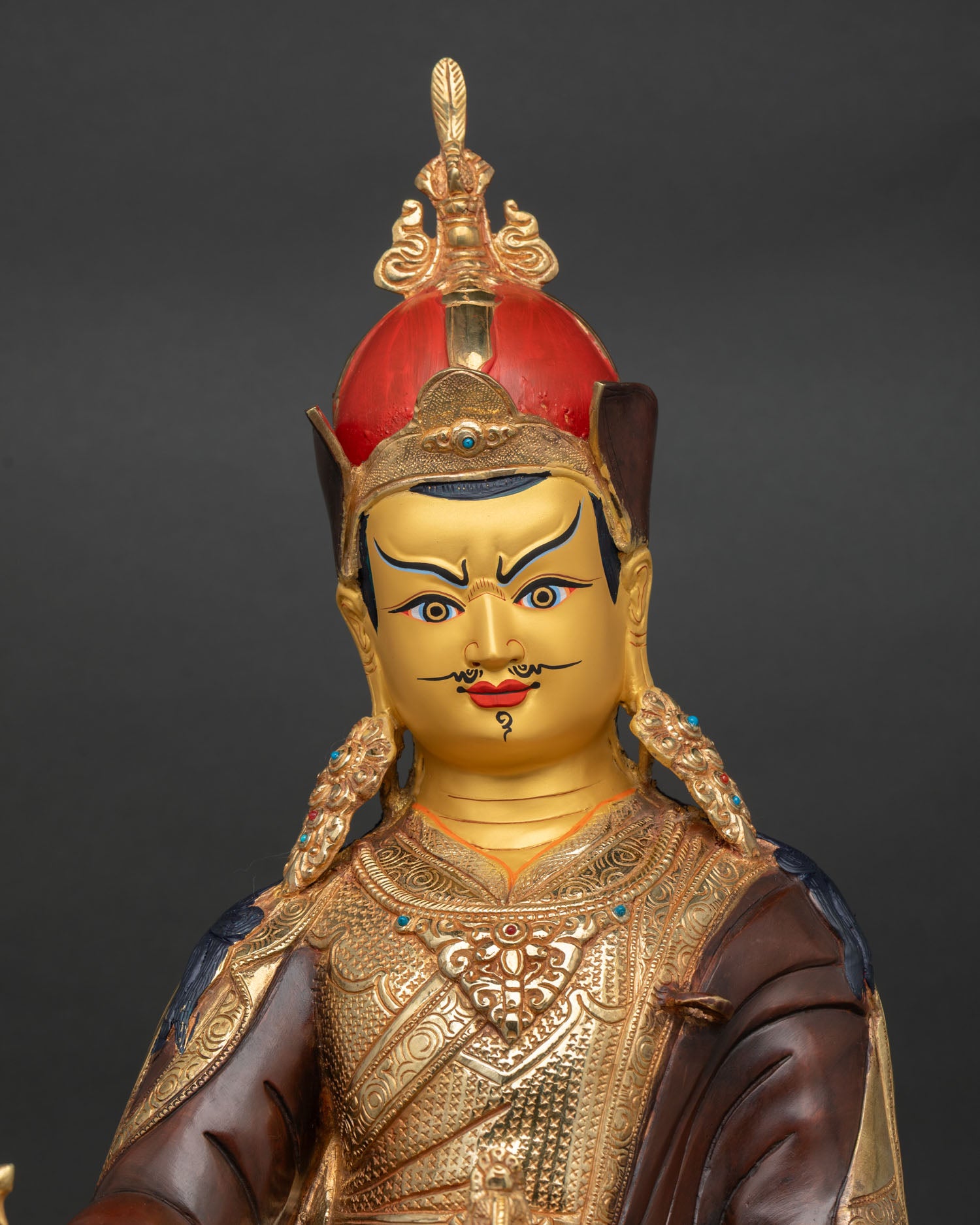 Close-up of Guru Rinpoche Statue showing gold-painted face, semi-wrathful expression, and ornaments.