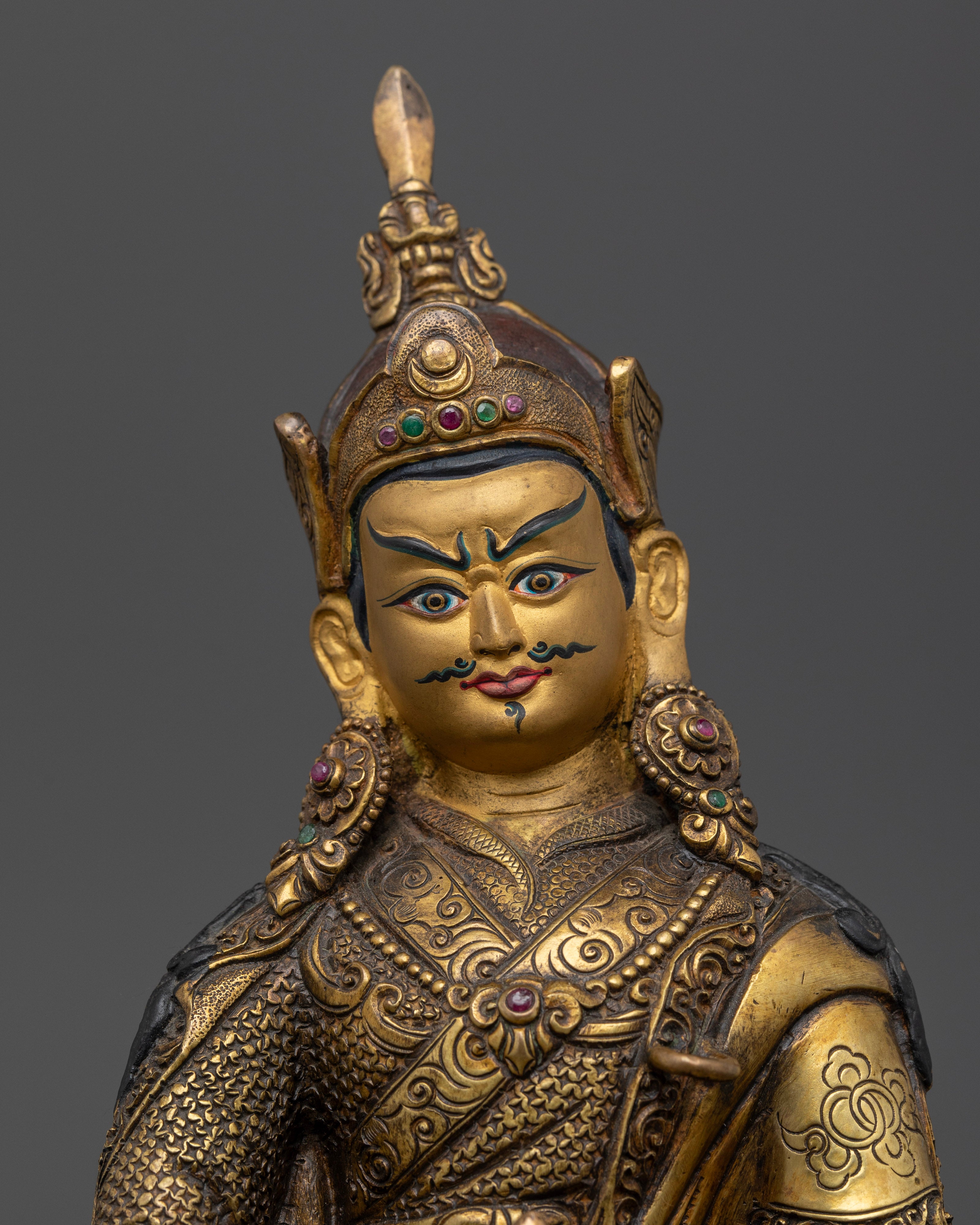 Close up of Guru Rinpoche statue with gold painted face and semi precious stone inlays