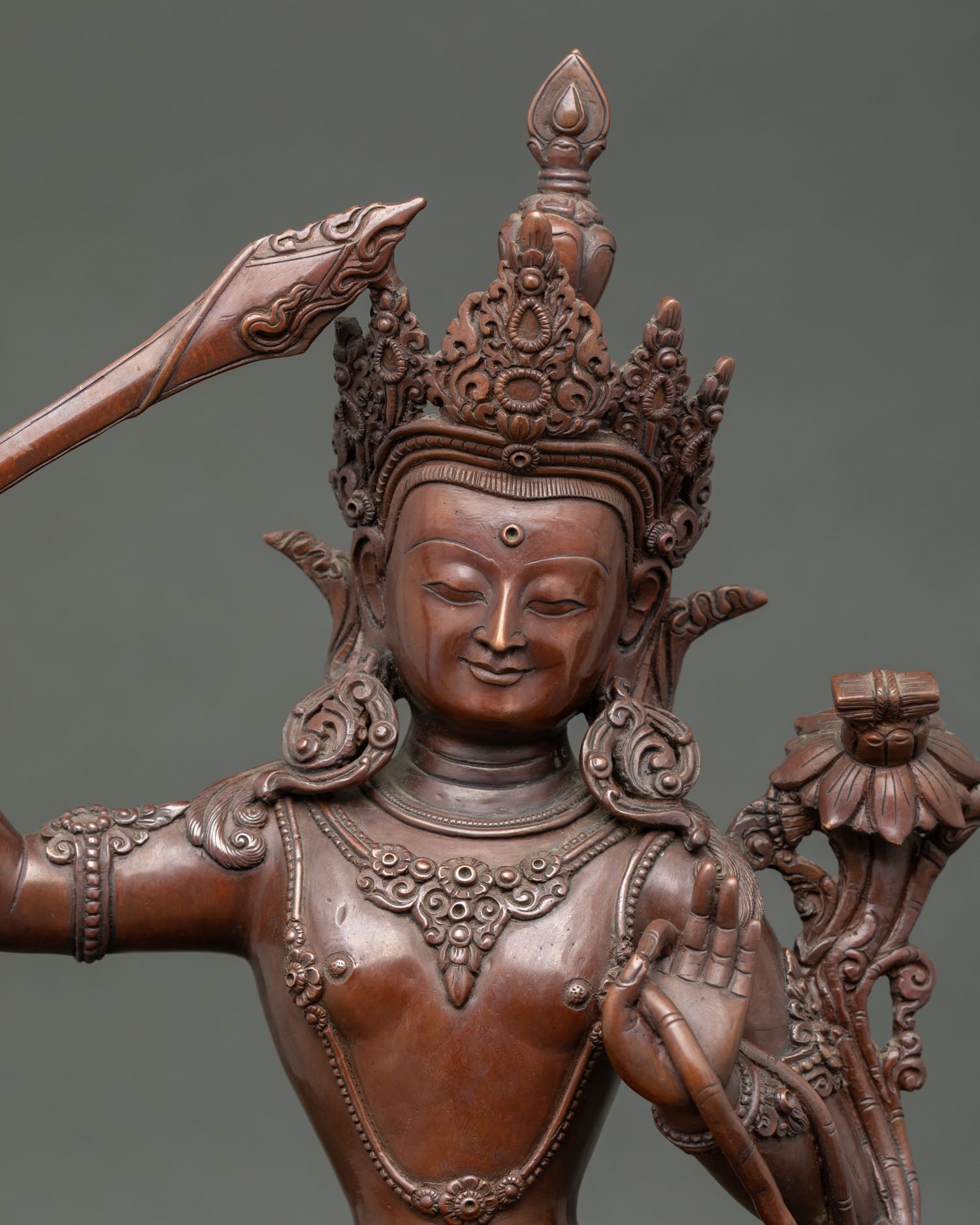 Close-up of handcrafted oxidized copper Manjushri figurine showing intricate 3D carving details and brownish patina finish