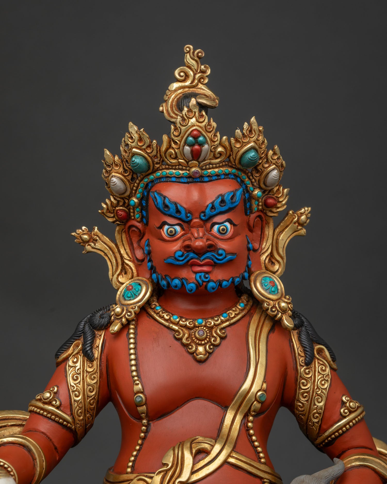 Close up of Jambhala Buddhist wealth deity holding a citron fruit and jewel mongoose with gold ornaments.
