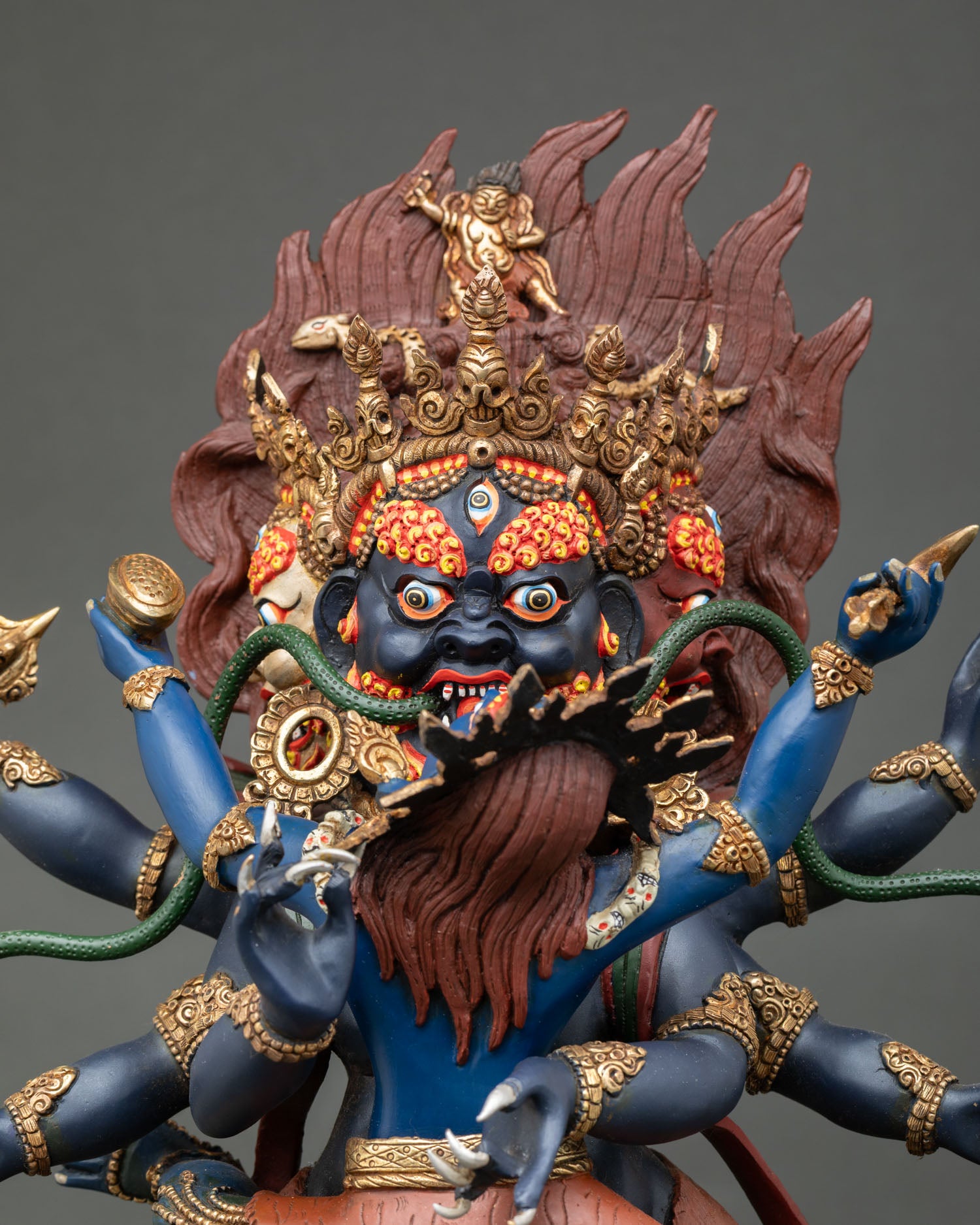 Close-up of Mahachakra Vajrapani sculpture showing three faces, five skull crown, intricate jewelry, and sacred Vajrayana details.