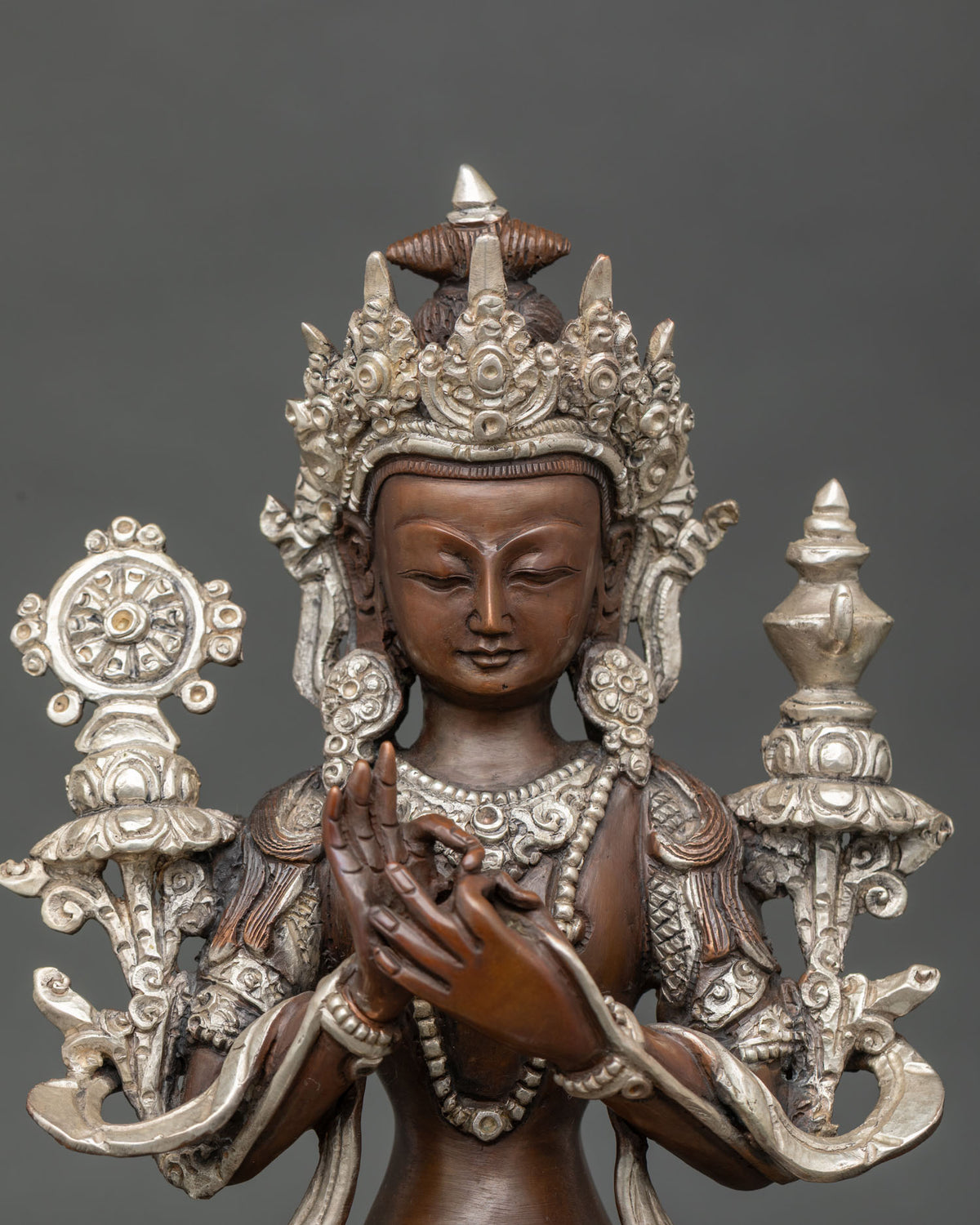 Close-up of Maitreya Buddha face, crown, and Dharma wheel on oxidized copper statue from Nepal