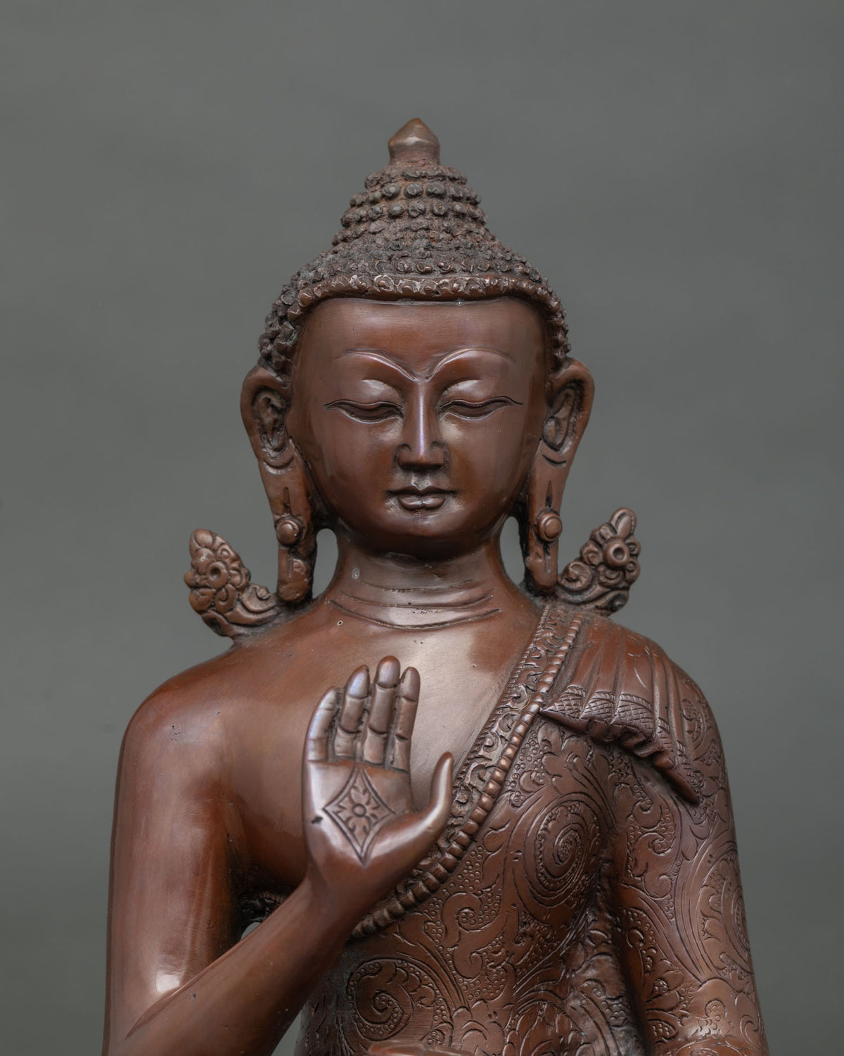 Close-up of oxidized copper Amoghasiddhi Buddha statue with raised hand and sacred bowl