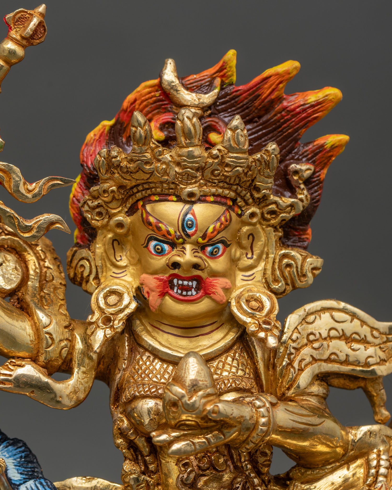 Close up of Palden Lhamo fierce face wide eyes bared teeth khatvanga staff skull cup copper gold painted sculpture