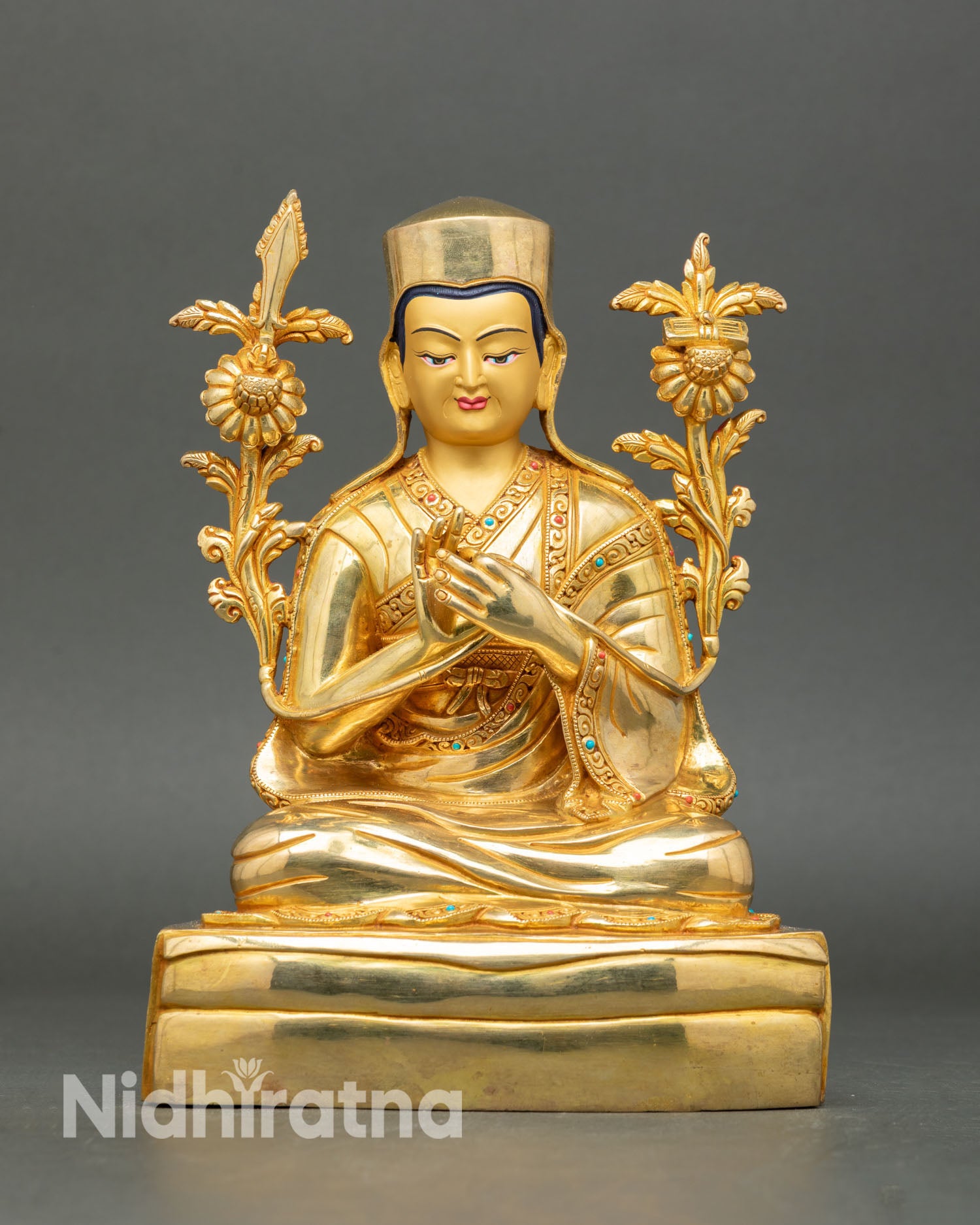Close up of Sakya Pandita statue showing gold gilded copper finish semi precious stone inlays and detailed lama robes in Himalayan Buddhist sculpture