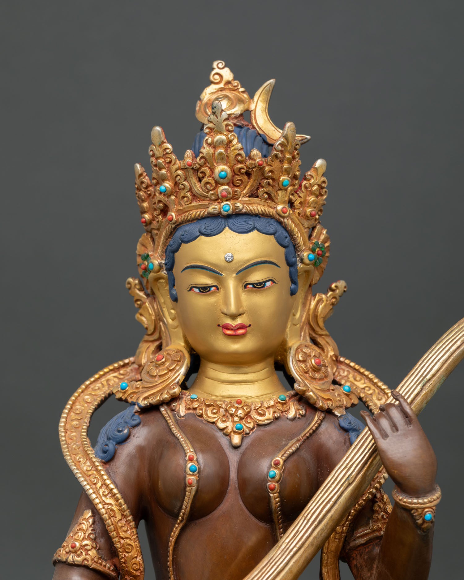 Close up of Saraswati statue with five jewel crown turquoise coral ornaments and shell motif.