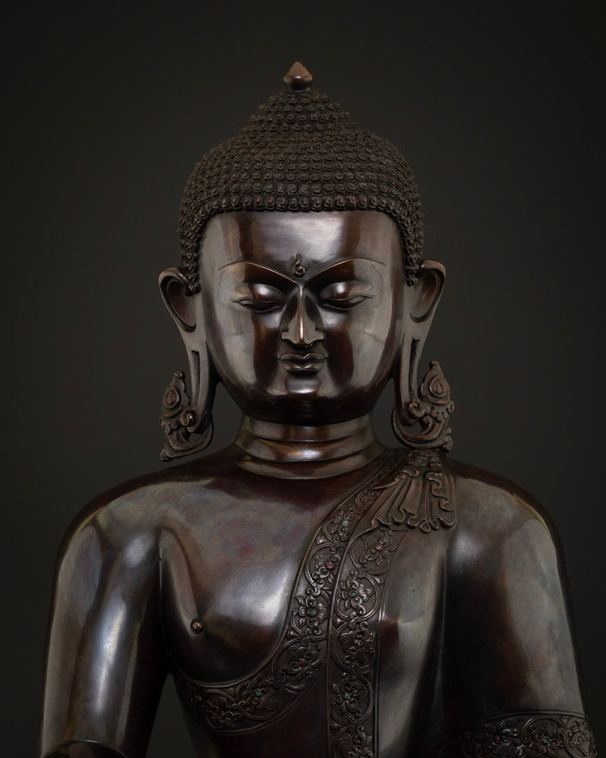 Close-up of serene Shakyamuni Buddha face, elaborate earrings and gemstone-adorned copper robe