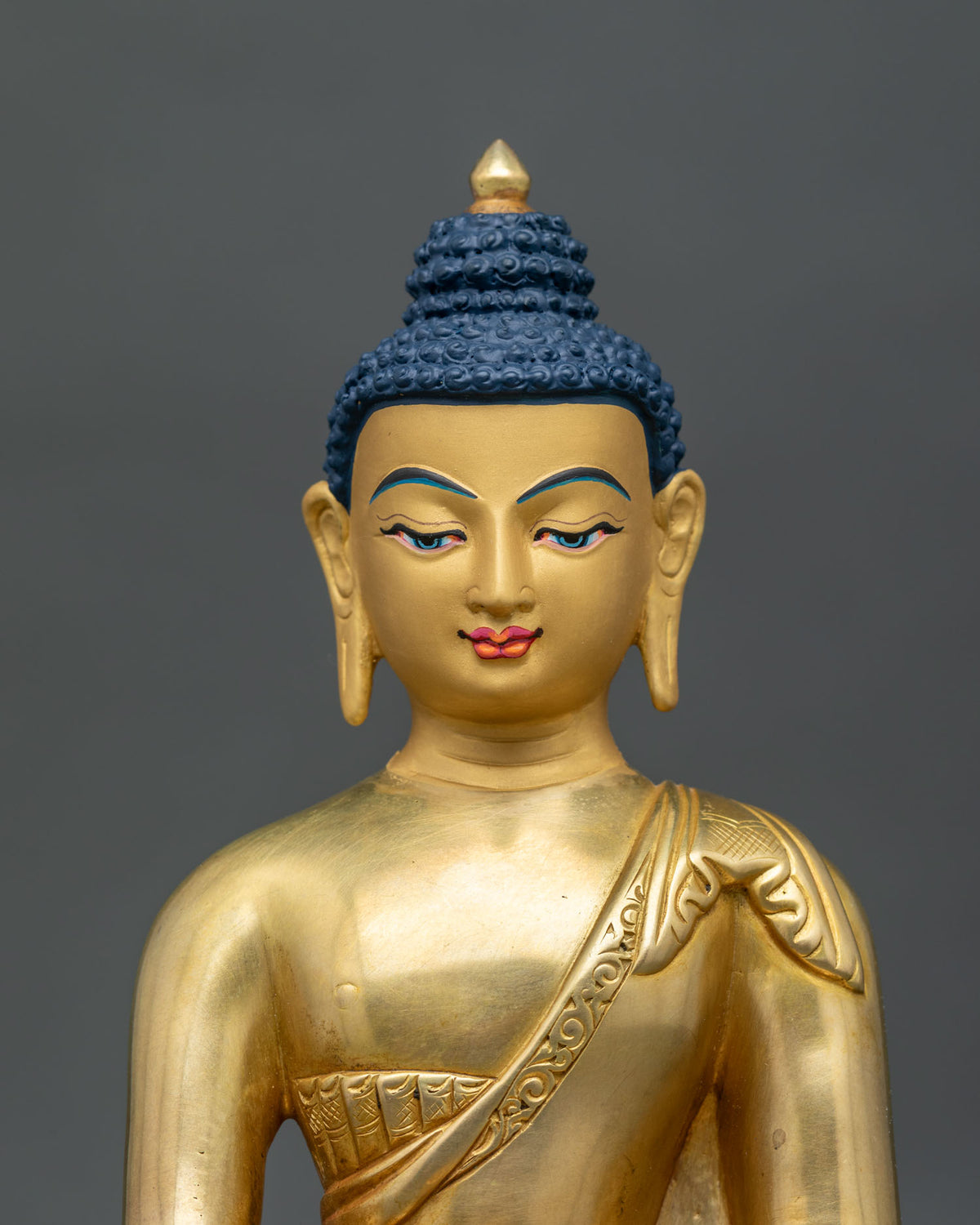 Close up of Shakyamuni buddha face with finely painted 24k gold details and monastic robe.