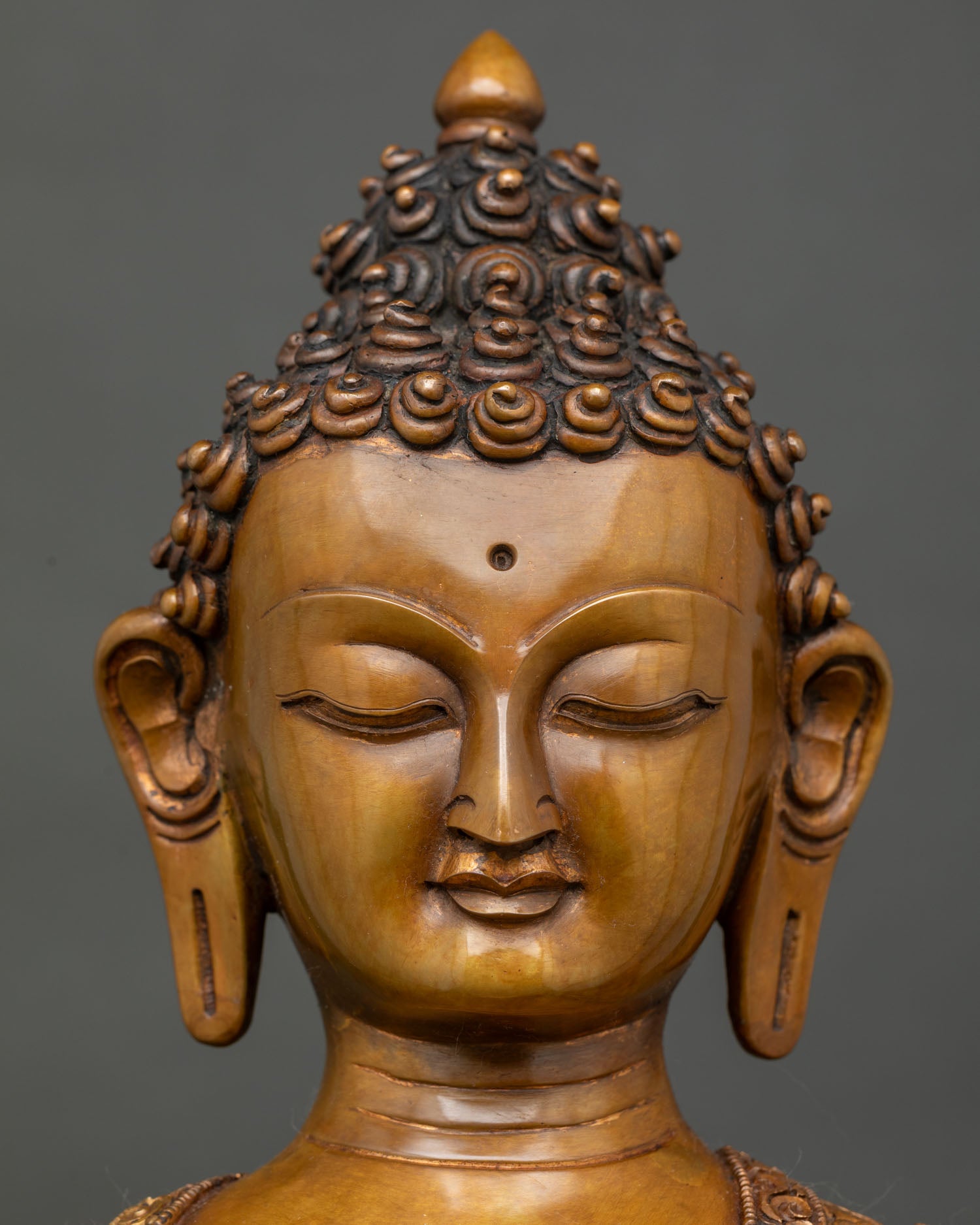 Close up of Shakyamuni Buddha face with serene expression elongated ears and warm brown oxidized finish