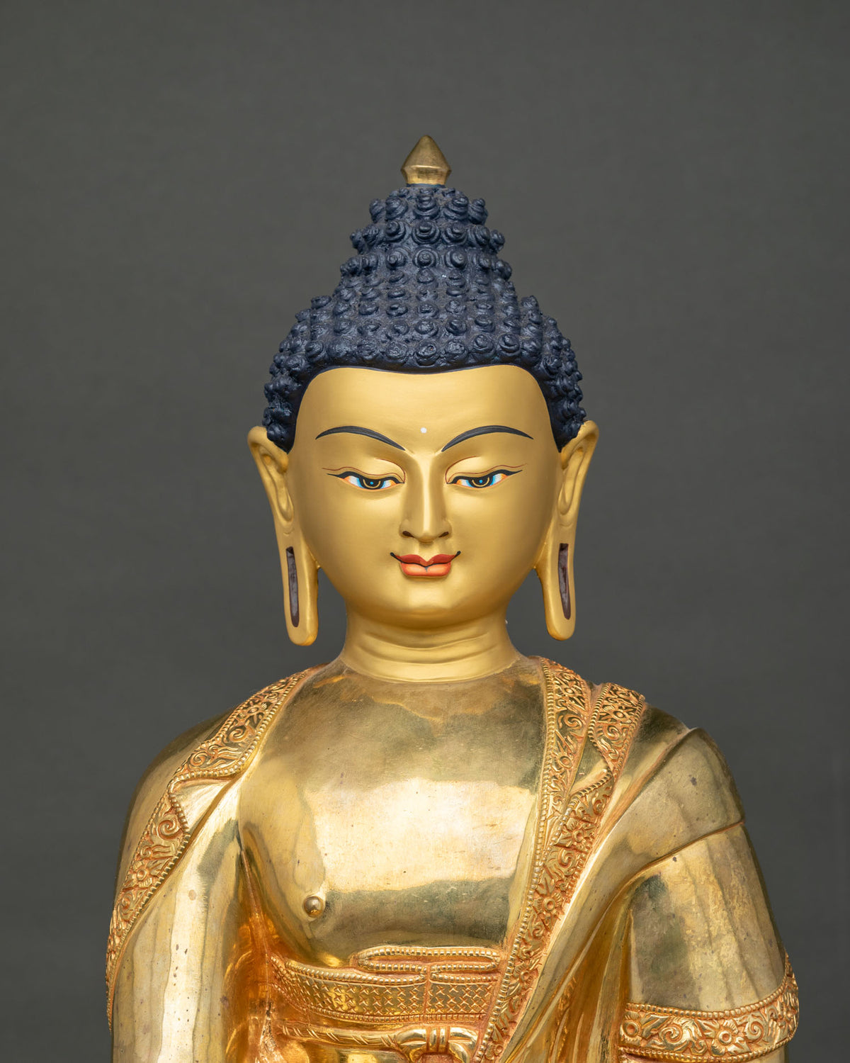 Close-up of Shakyamuni Buddha statue head and chest with fine robe engraving in 24K gold gilding