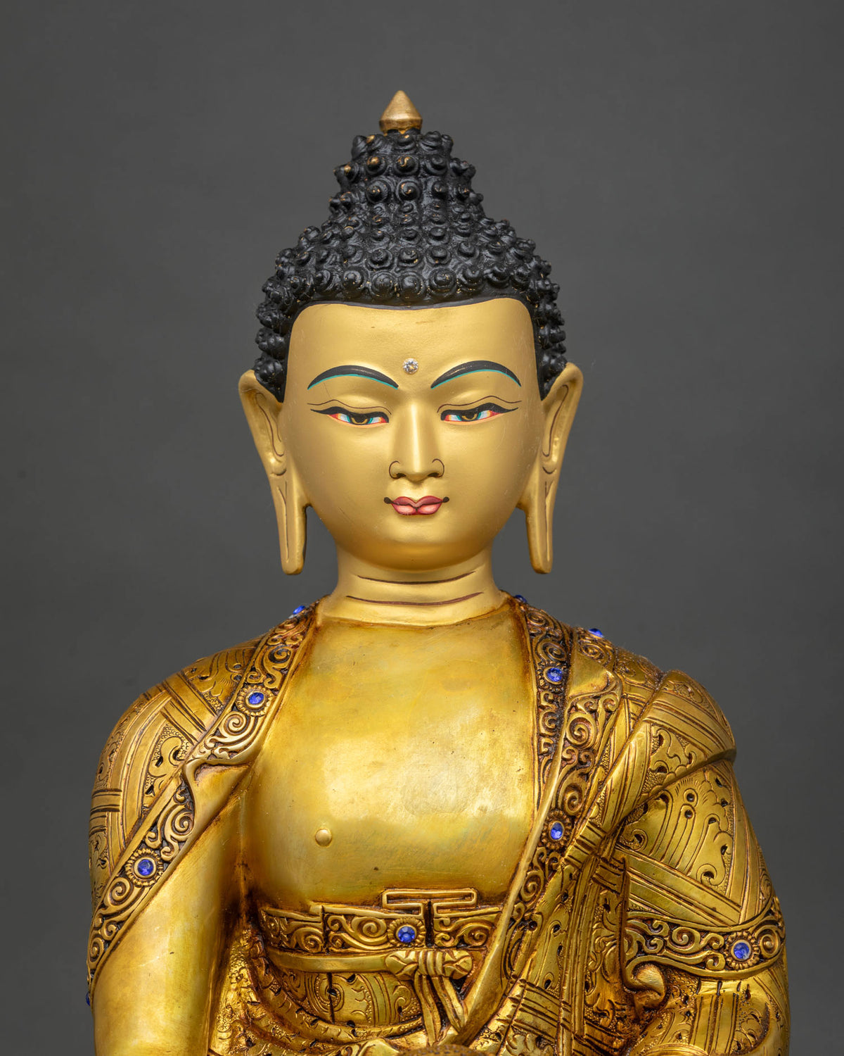 Close up of Shakyamuni Buddha statue upper body with gemstone inlays and engraved monastic robe