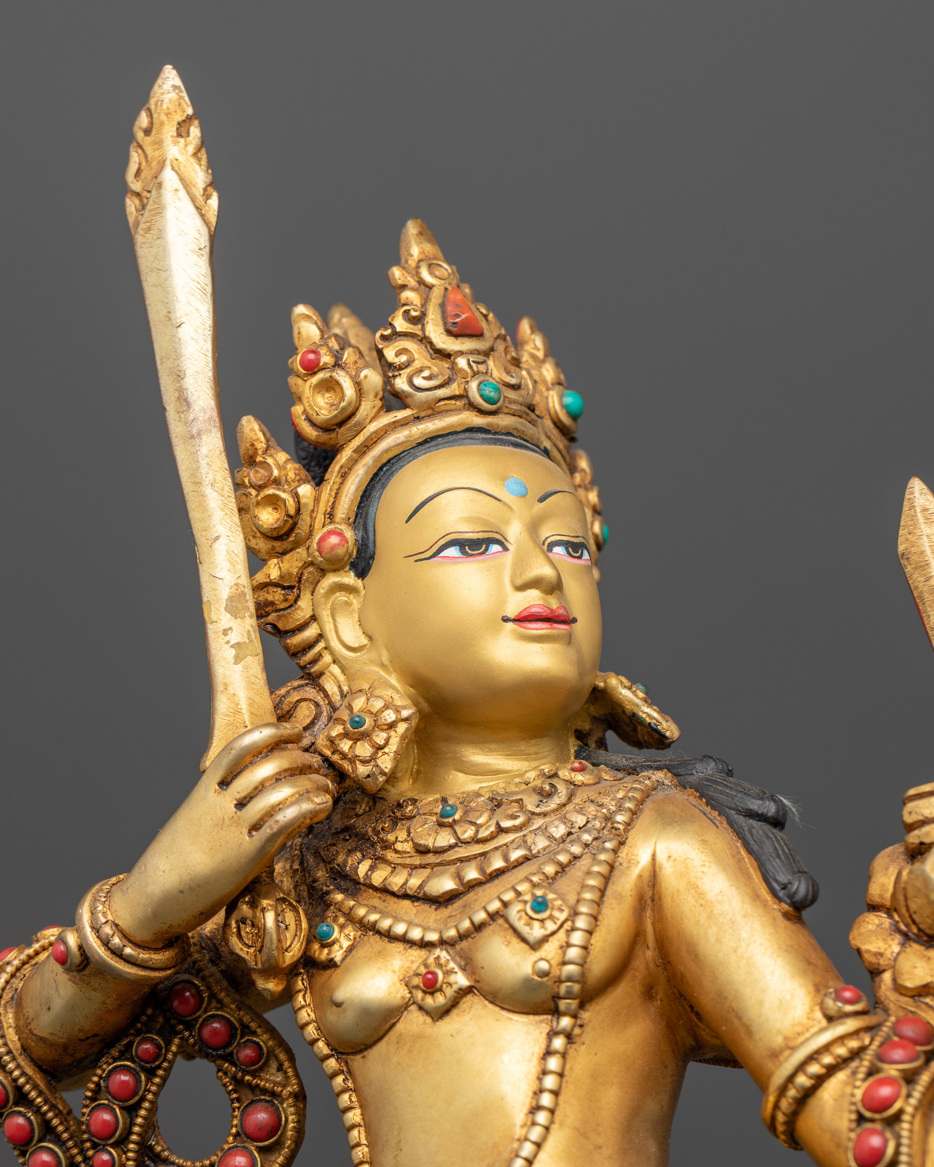 Close up Standing Manjushri statue with gold painted face and filigree artwork.
