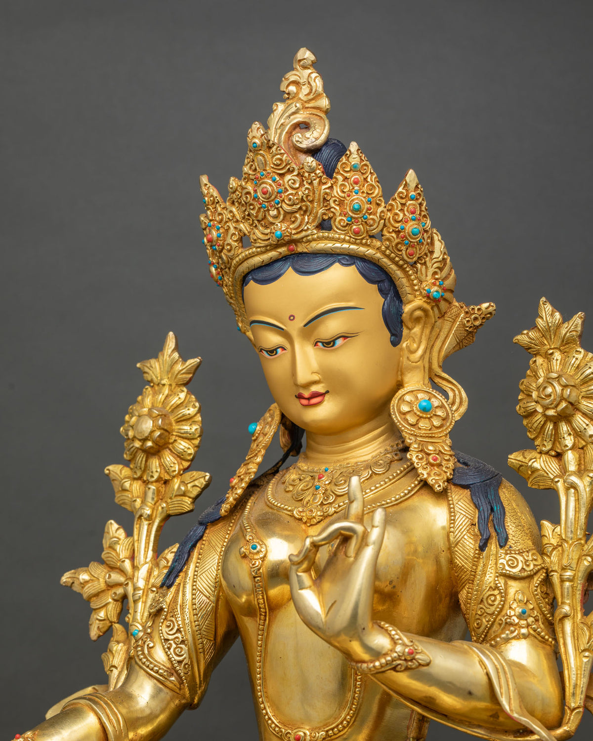 Close-up of the Tara face with a turquoise and coral inlaid crown and earrings on a gold gilded statue