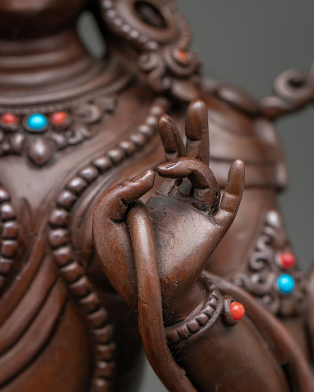 Close-up of Tibetan Green Tara statue hand gesture with coral and turquoise accents