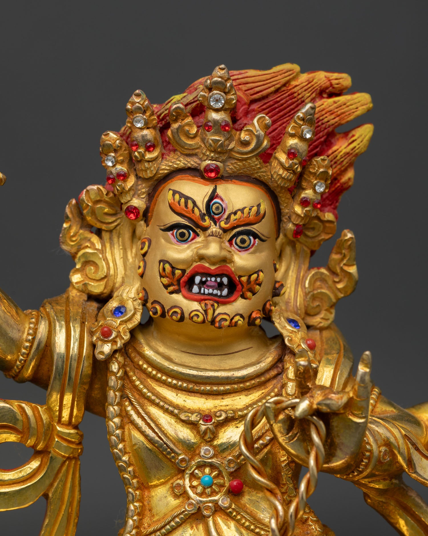 Close up of Vajrapani statue with gold painted face and semi precious stone ornaments