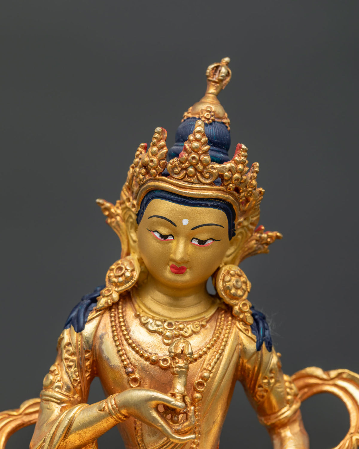 Close up of Vajrasattva statue with 24K gold painted face five jewel crown and serene expression.