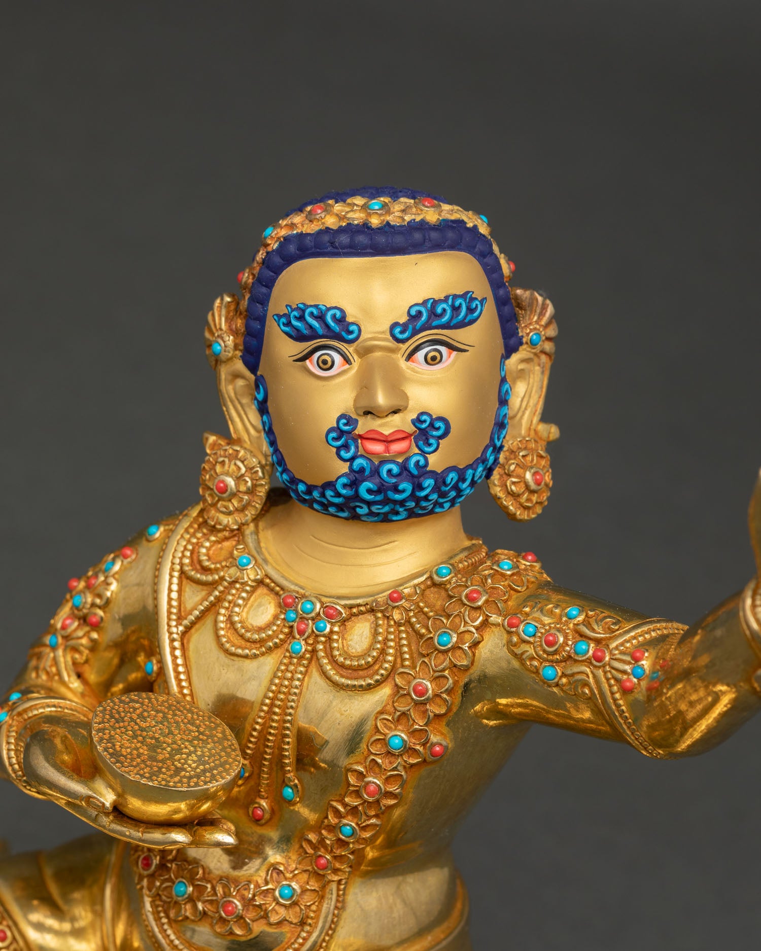 Close up of Virupa statue with gold painted face and serene tantric expression holding skull cup