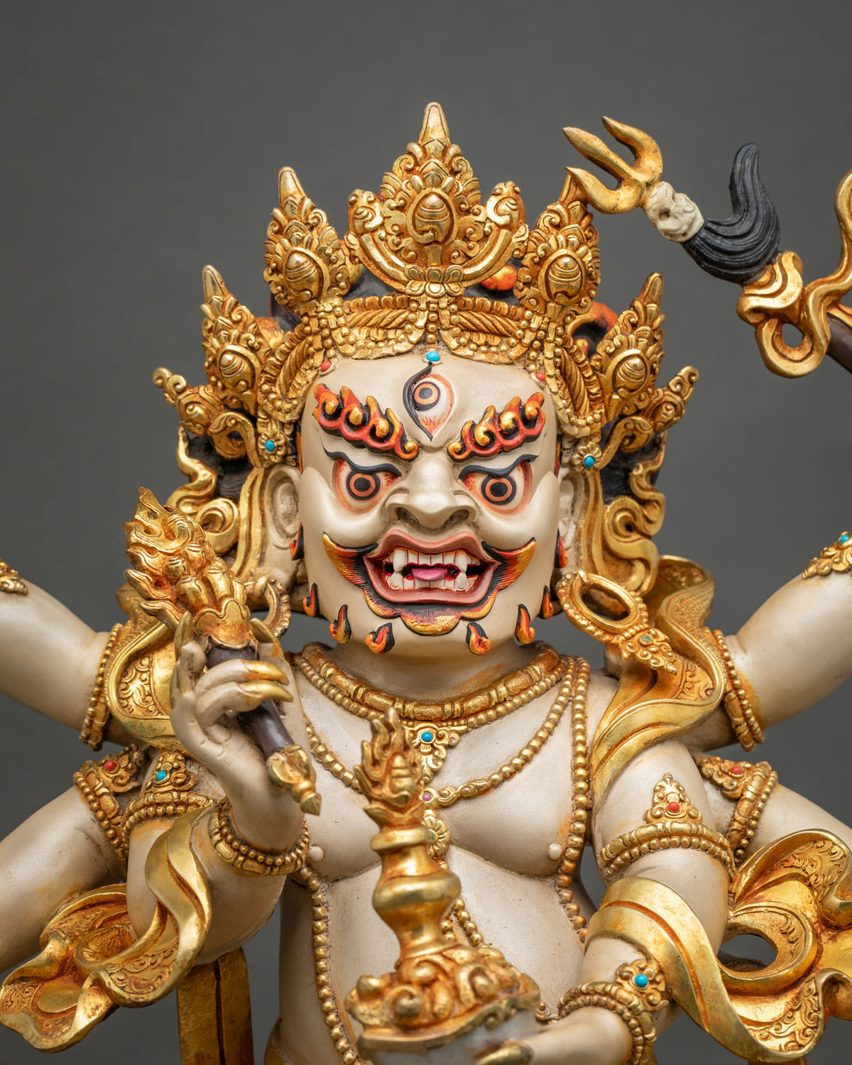 Close-up of White Mahakala statue with fierce three-eyed face, ornate gilded crown, gold garments