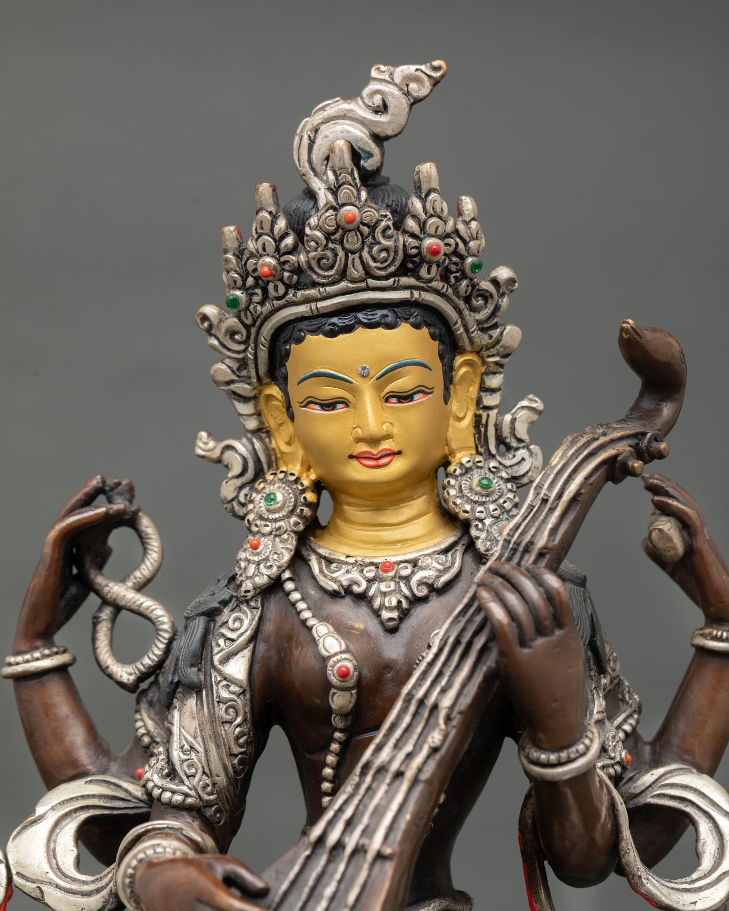 Close up Saraswati face gold finish serene expression Hindu Goddess sculpture with stones for knowledge inspiration