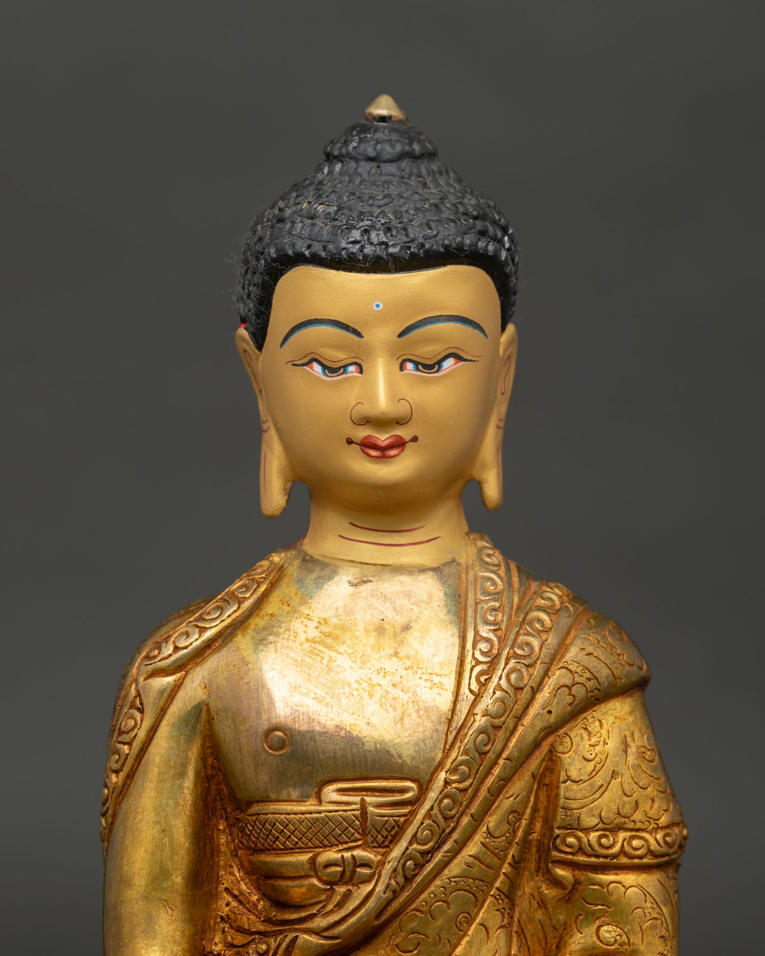 Close up Shakyamuni Buddha statue showing gold painted face floral monk robe and intricate details.