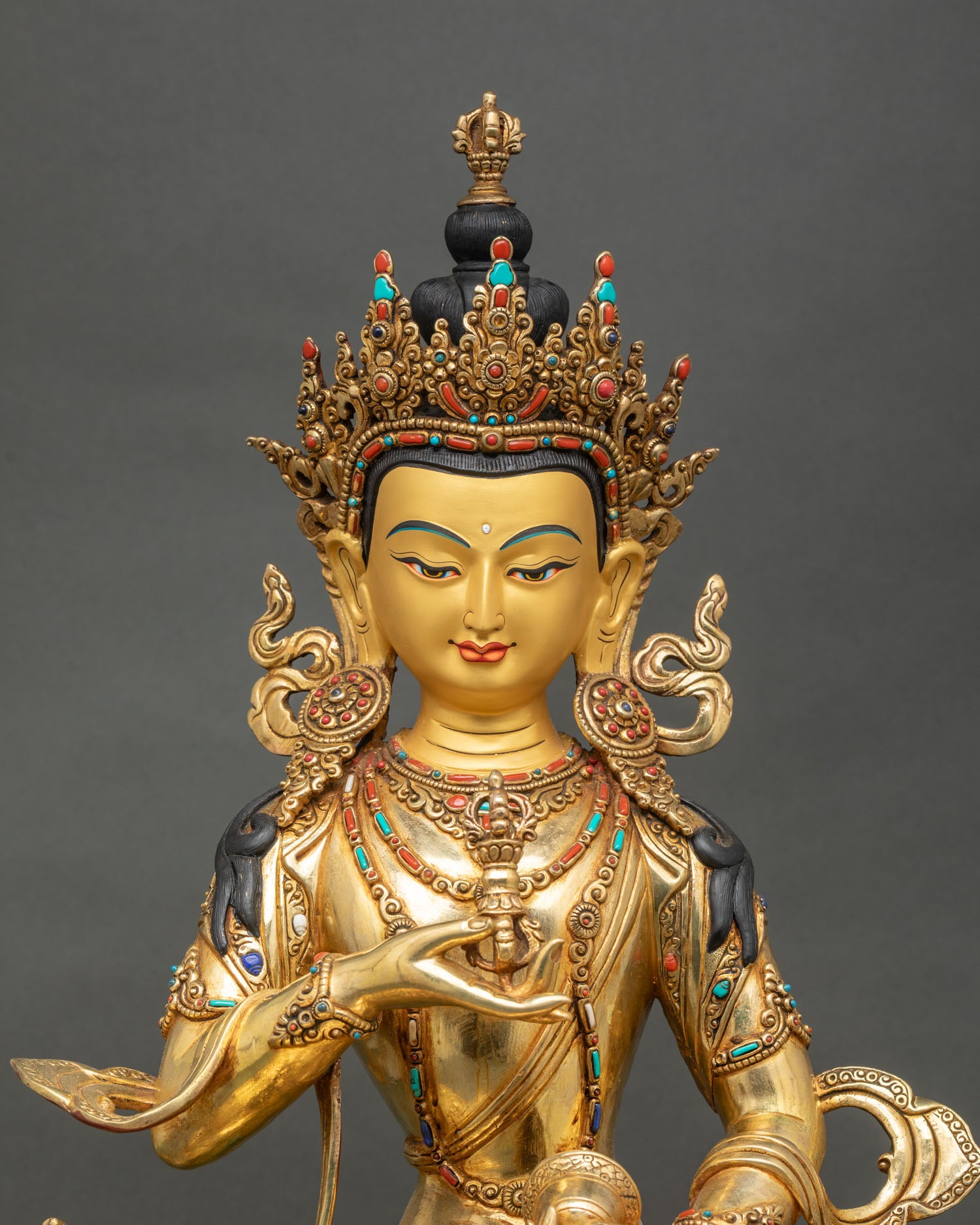 Close up of Vajrasattva statue showing gold painted face, holding Vajra and Ghanta, symbolizing spiritual blessings.