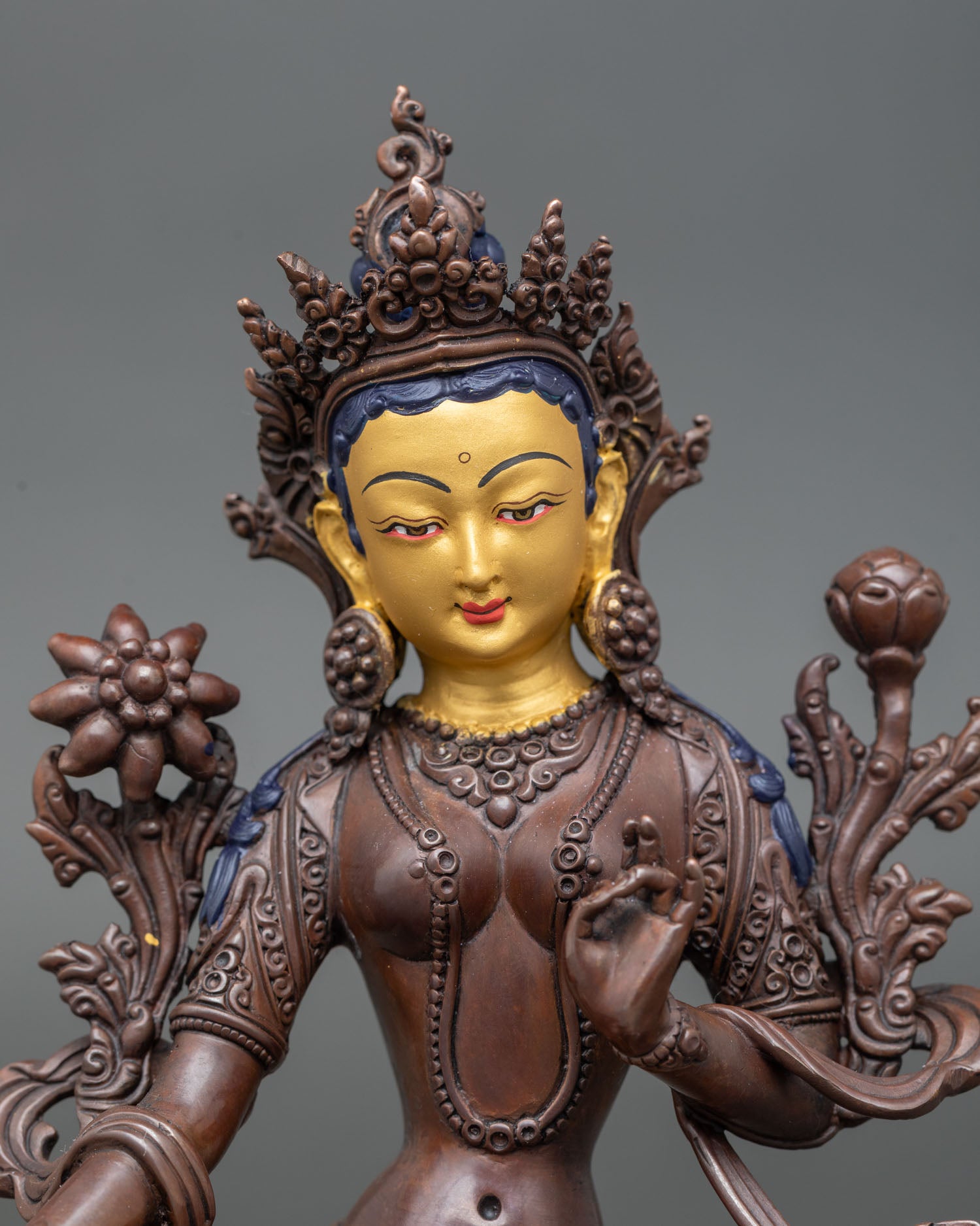Close up view Green Tara face with gold painted detail oxidized copper Buddhist statue symbol of compassion protection and liberation Himalayan sacred art from Nepal