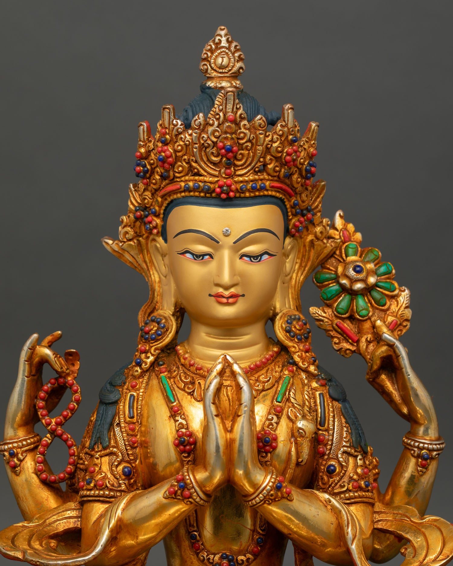 Close-up view of Chenrezig statue with a serene gold painted face, an ornate crown, and detailed semi-precious stone embellishments