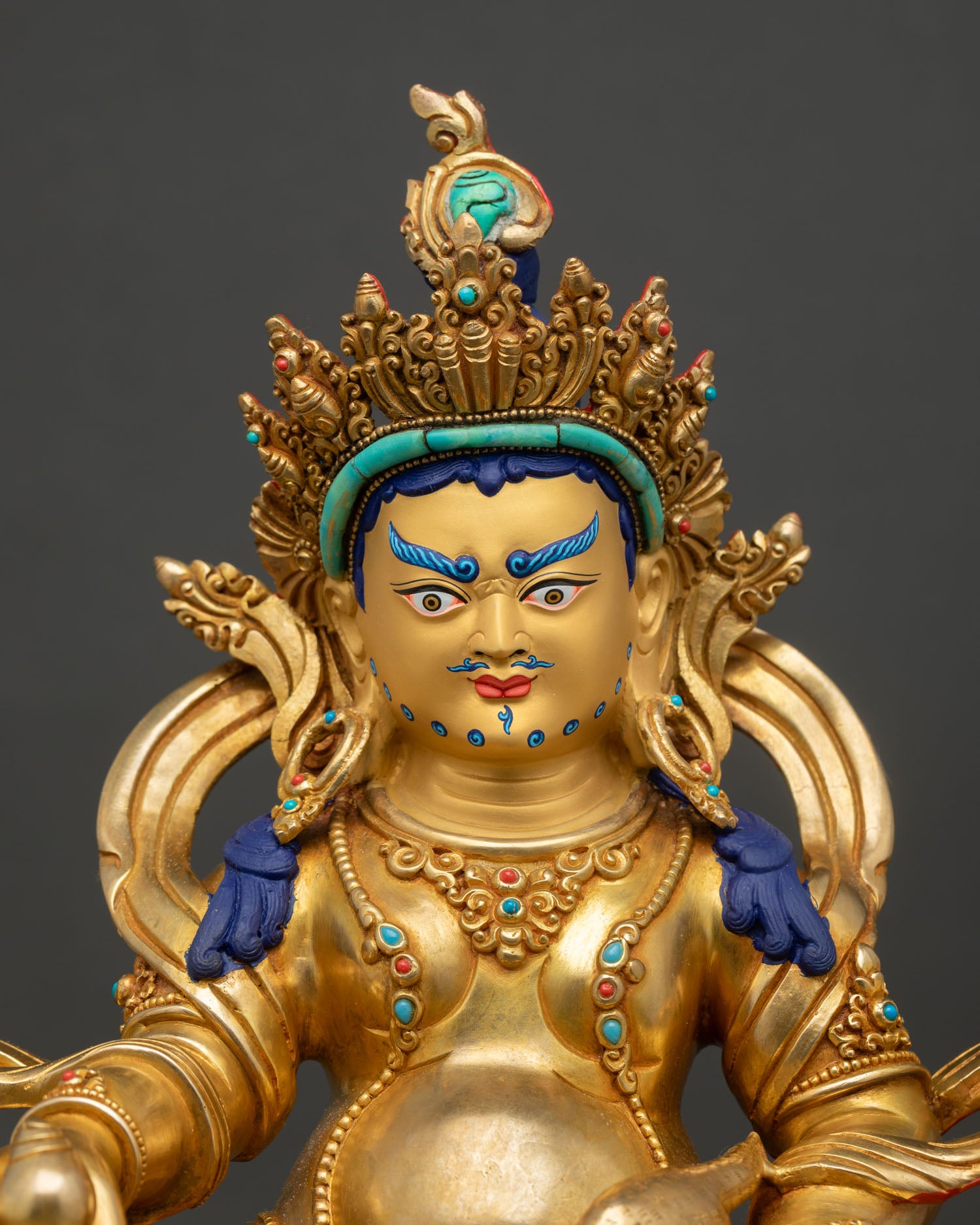 Close up view of Dzambhala Statue showing gold painted face, jeweled crown, turquoise stones, and detailed ornaments