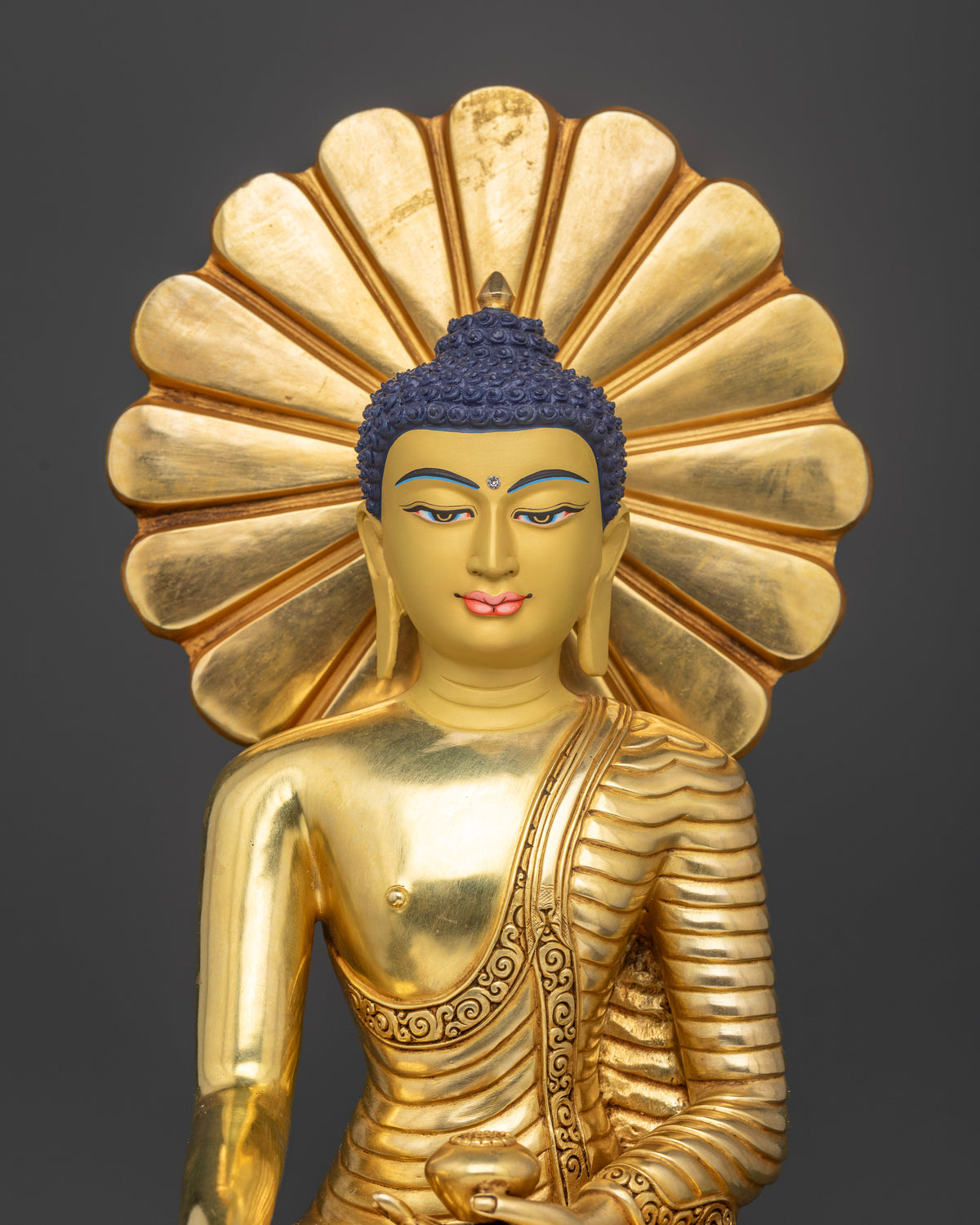 Close-up view of gold-gilded Shakyamuni Buddha statue showing detailed monastic robes, floral patterns, and turquoise halo accents
