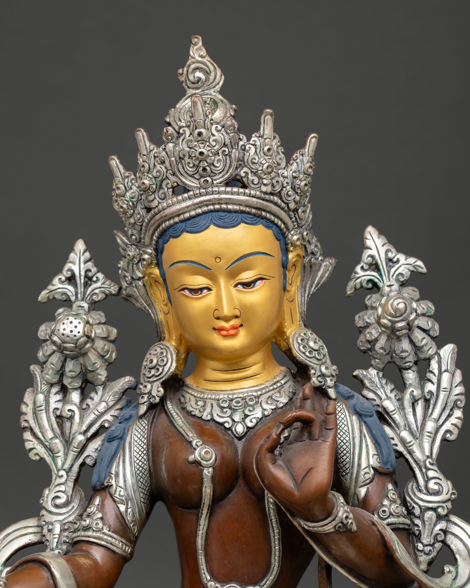 Close up view of Green Tara Buddhist sculpture, showing serene gold painted face and intricate Nepalese craftsmanship