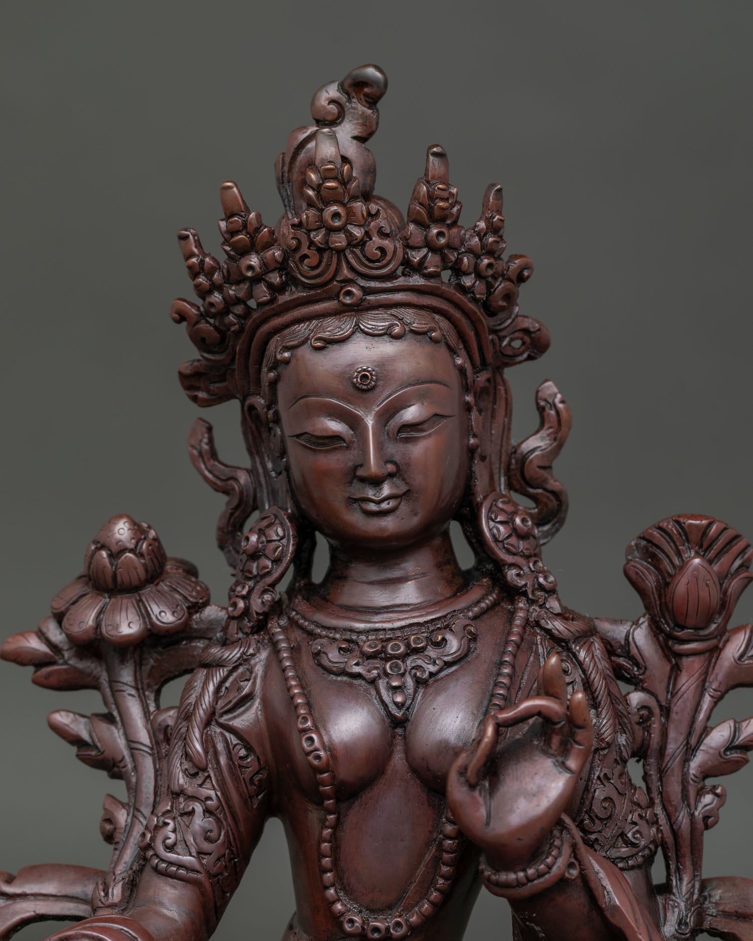 Close up view of Green Tara face and intricate jewelry details on oxidized copper statue.