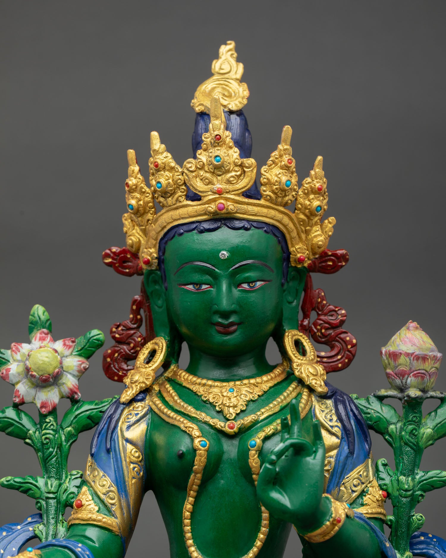 Close up view of Green Tara statue showing serene expression intricate carvings and gold gilded sacred facial details.