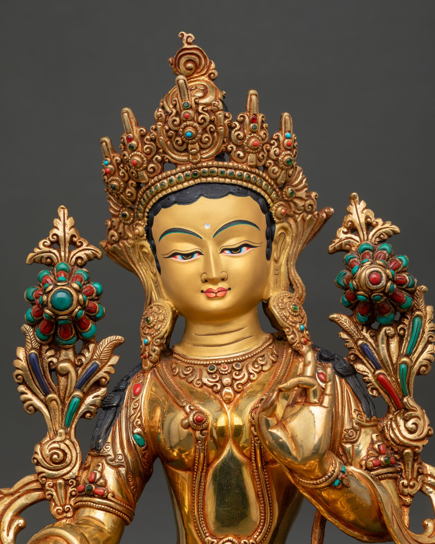 Close-up view of Green Tara statue, highlighting serene gold painted face, compassionate expression, and stone detailing 