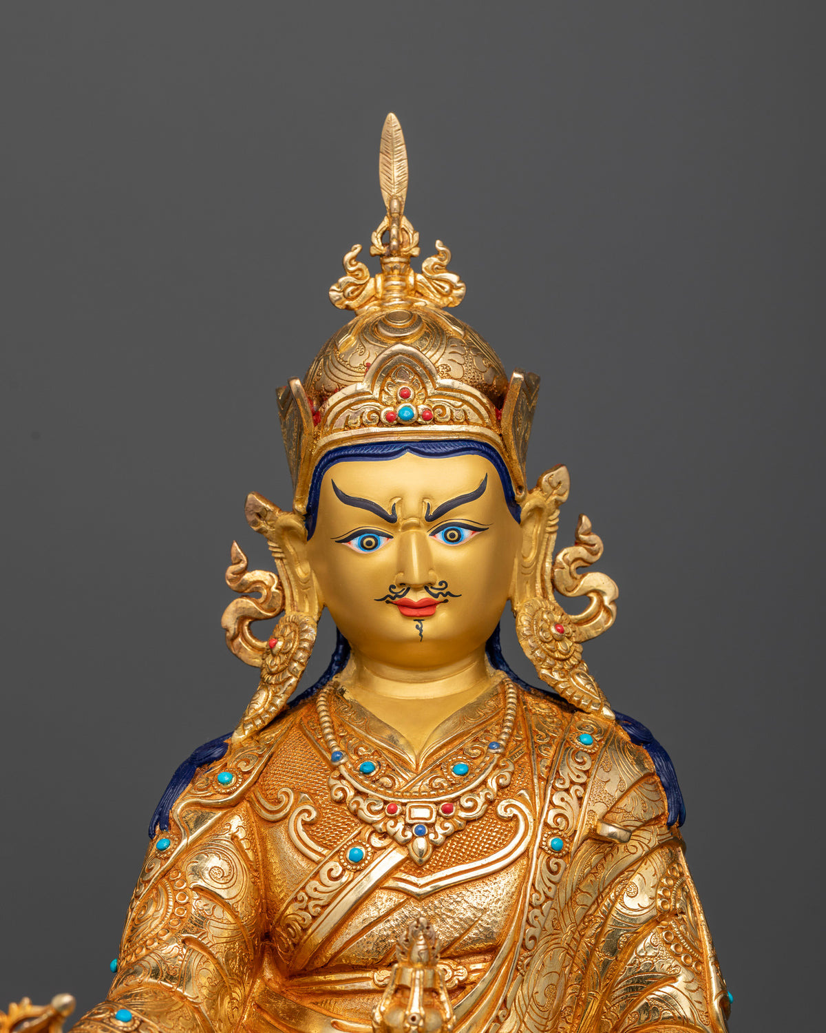 Close-up view of Guru Rinpoche statue featuring lotus hat, gold-painted face, and gemstone adornments.