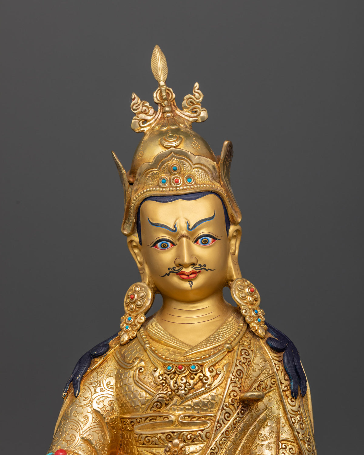 Close-up view of Guru Rinpoche statue showcasing a gold-painted face, ornate Buddhist details, and semi-precious gemstone inlays