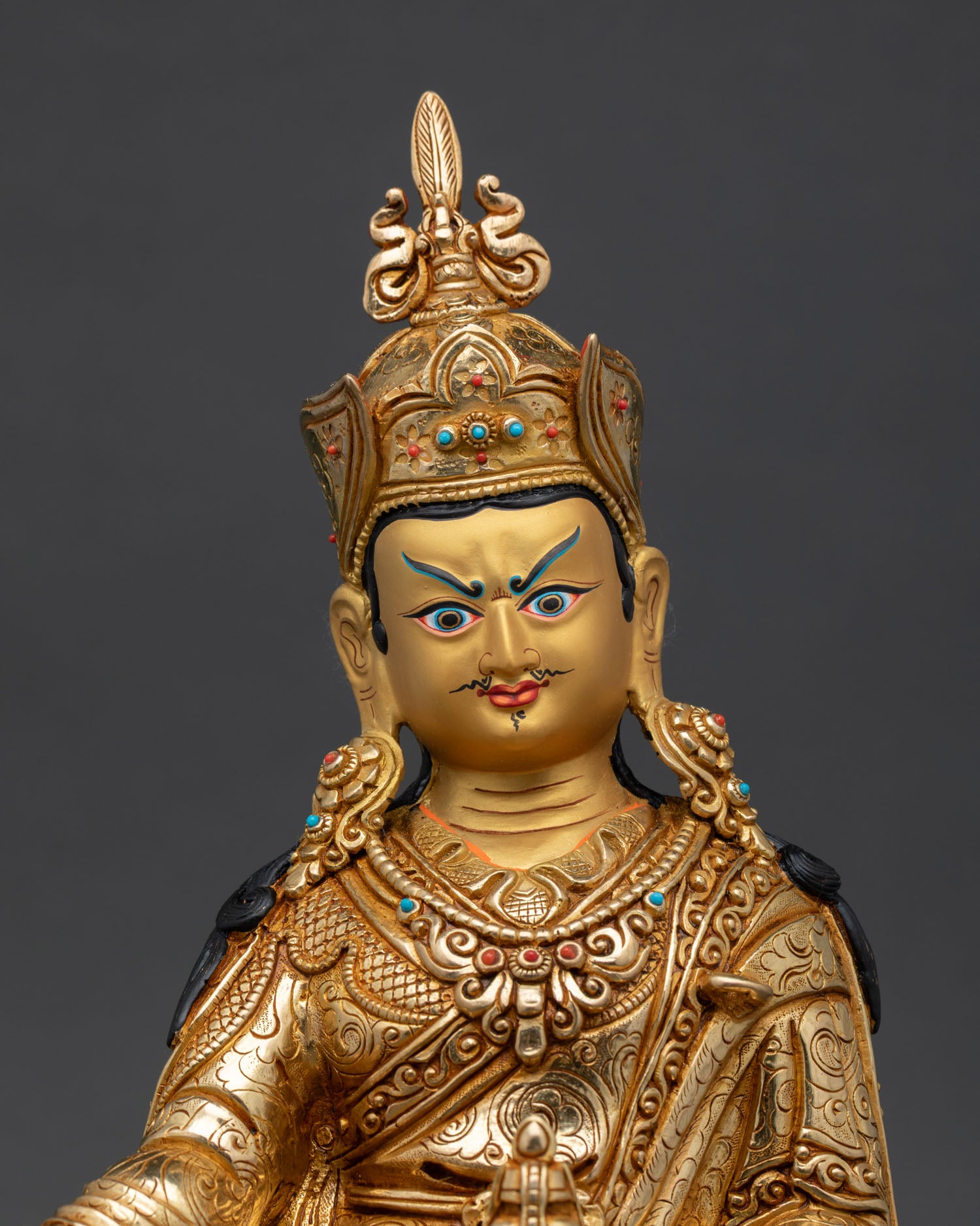 Close up view of Guru Rinpoche statue showing detailed gold painted face and semi precious stone embellishments with sacred Himalayan craftsmanship