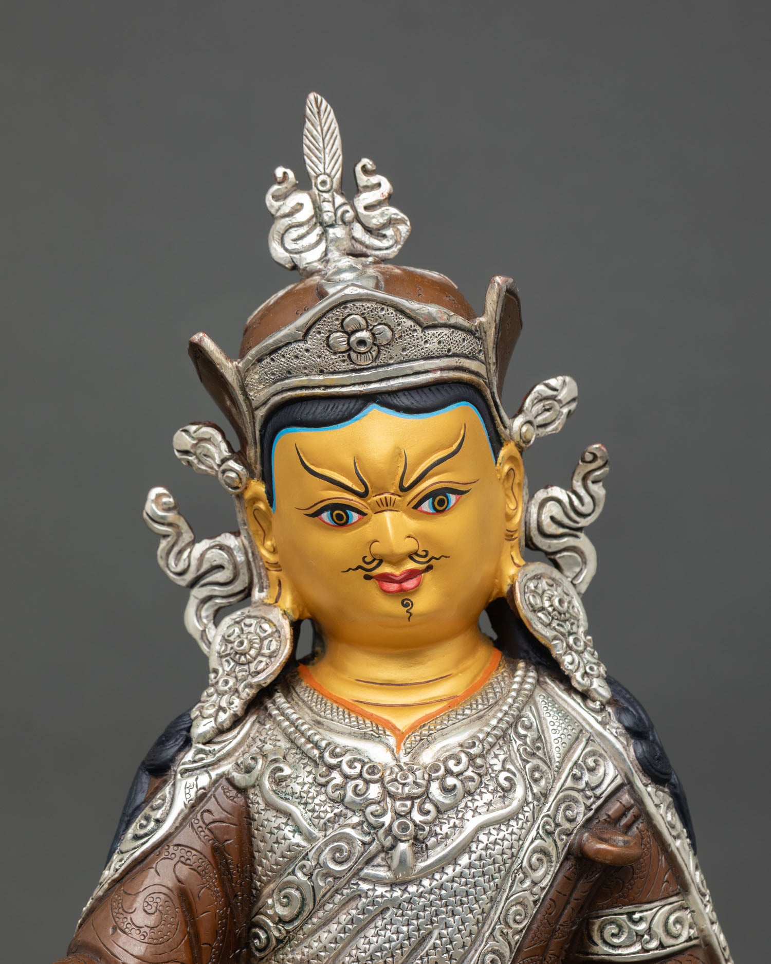 Close-up view of the Guru Rinpoche statue with a serene gold-painted face, a lotus hat, a feather crown, and detailed Himalayan craftsmanship