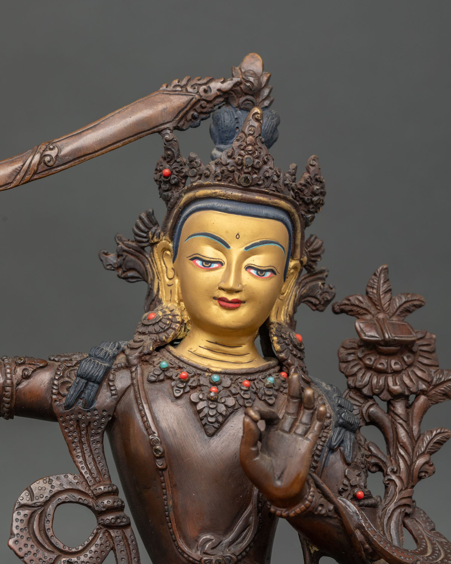 Close up view of Manjushri statue with gold painted face gemstones and hand carved silk garment.