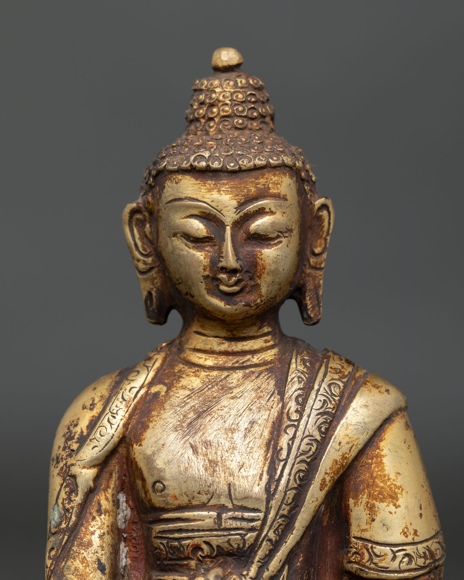 Close-up view of Medicine Buddha gold gilded face and peaceful compassionate expression.