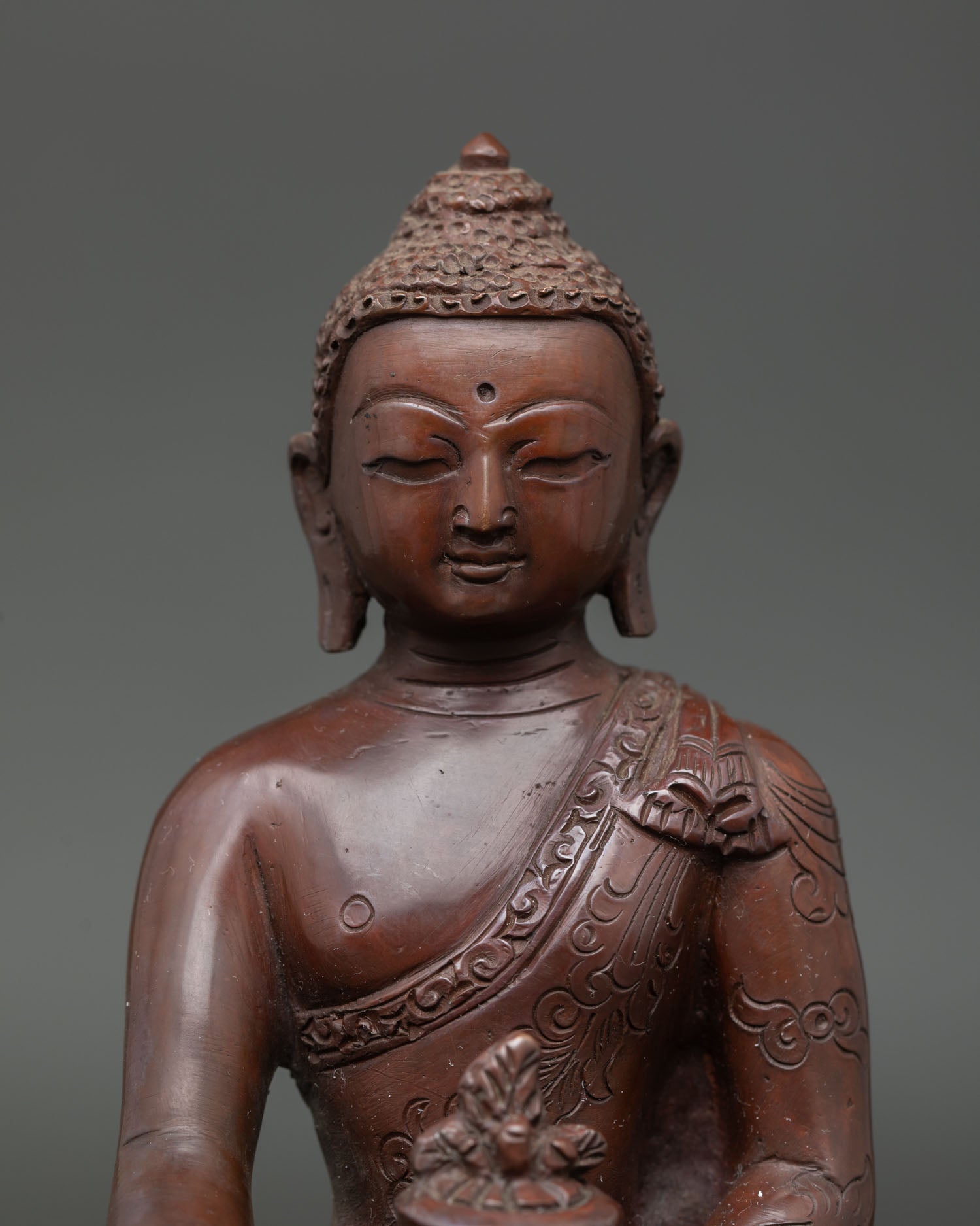 Close up view of Medicine Buddha holding a myrobalan plant in the right hand, finely detailed copper sculpture crafted in Patan Nepal with traditional Buddhist artistry.